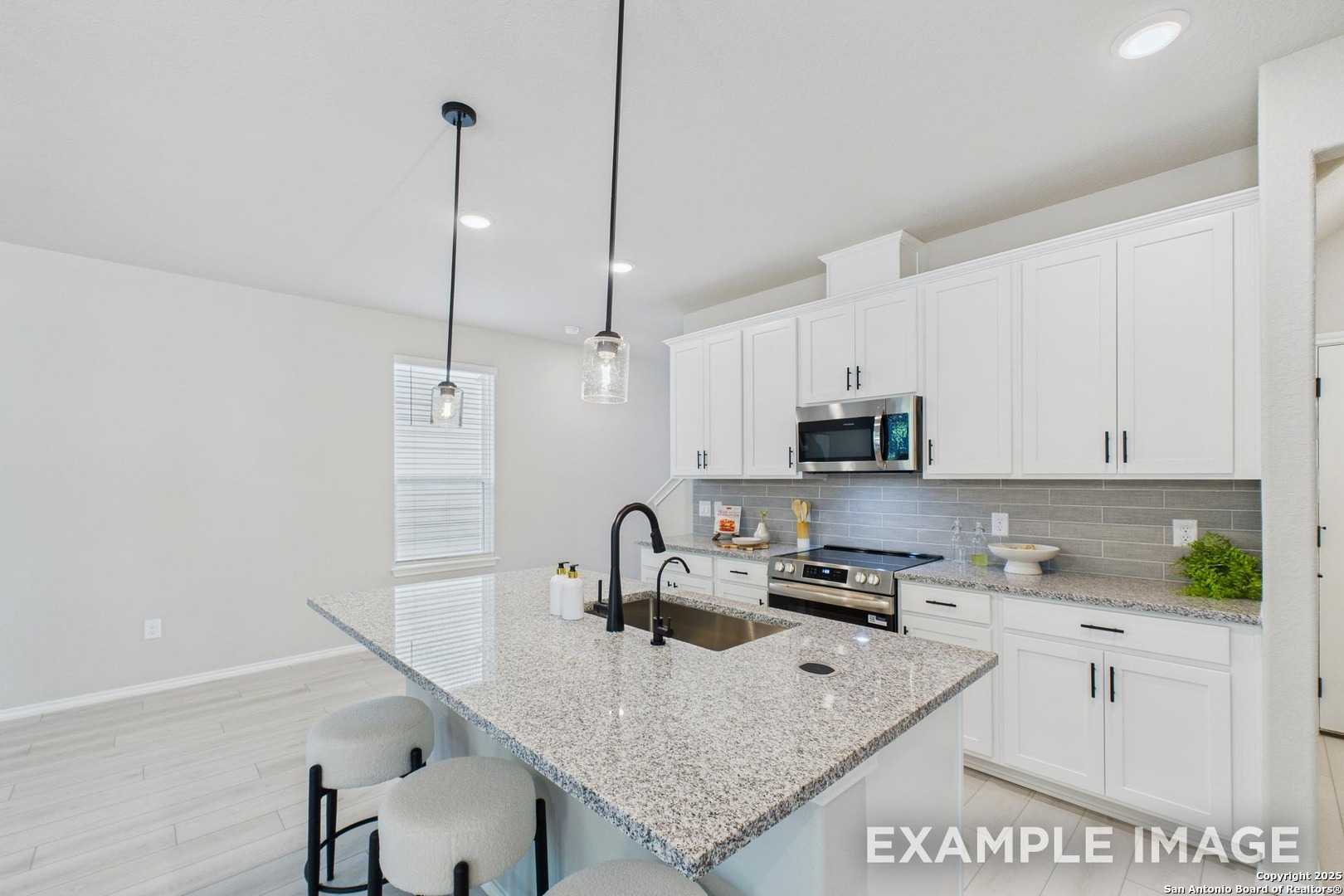 Modern kitchen featuring granite island, white cabinets, stainless appliances, and pendant lights in The Charlotte A by Davidson Homes, San Antonio