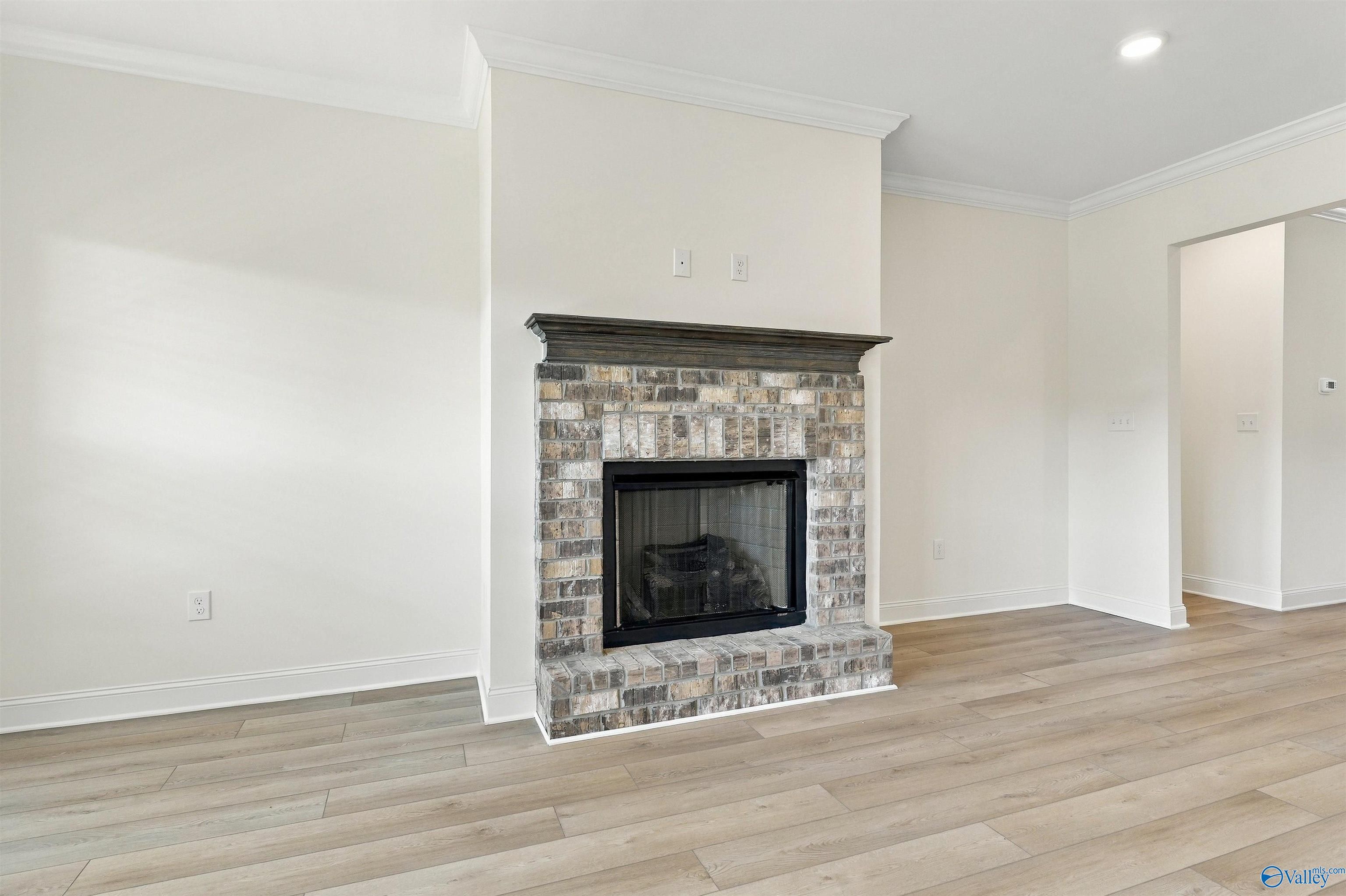 Brick fireplace with dark wood mantel in bright living room with hardwood floors in Davidson Homes Valencia, Huntsville, AL