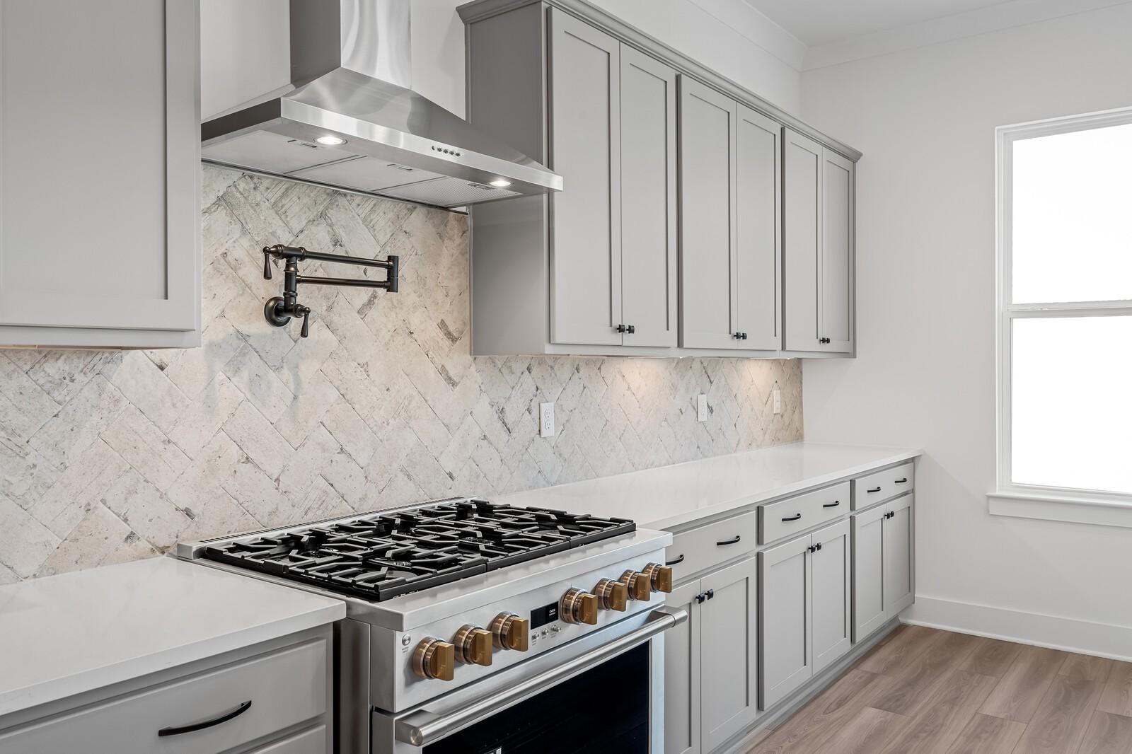 Modern kitchen with light gray shaker cabinets, herringbone subway tile backsplash, white quartz counters, and stainless gas range in The Alston A, Murfreesboro, TN