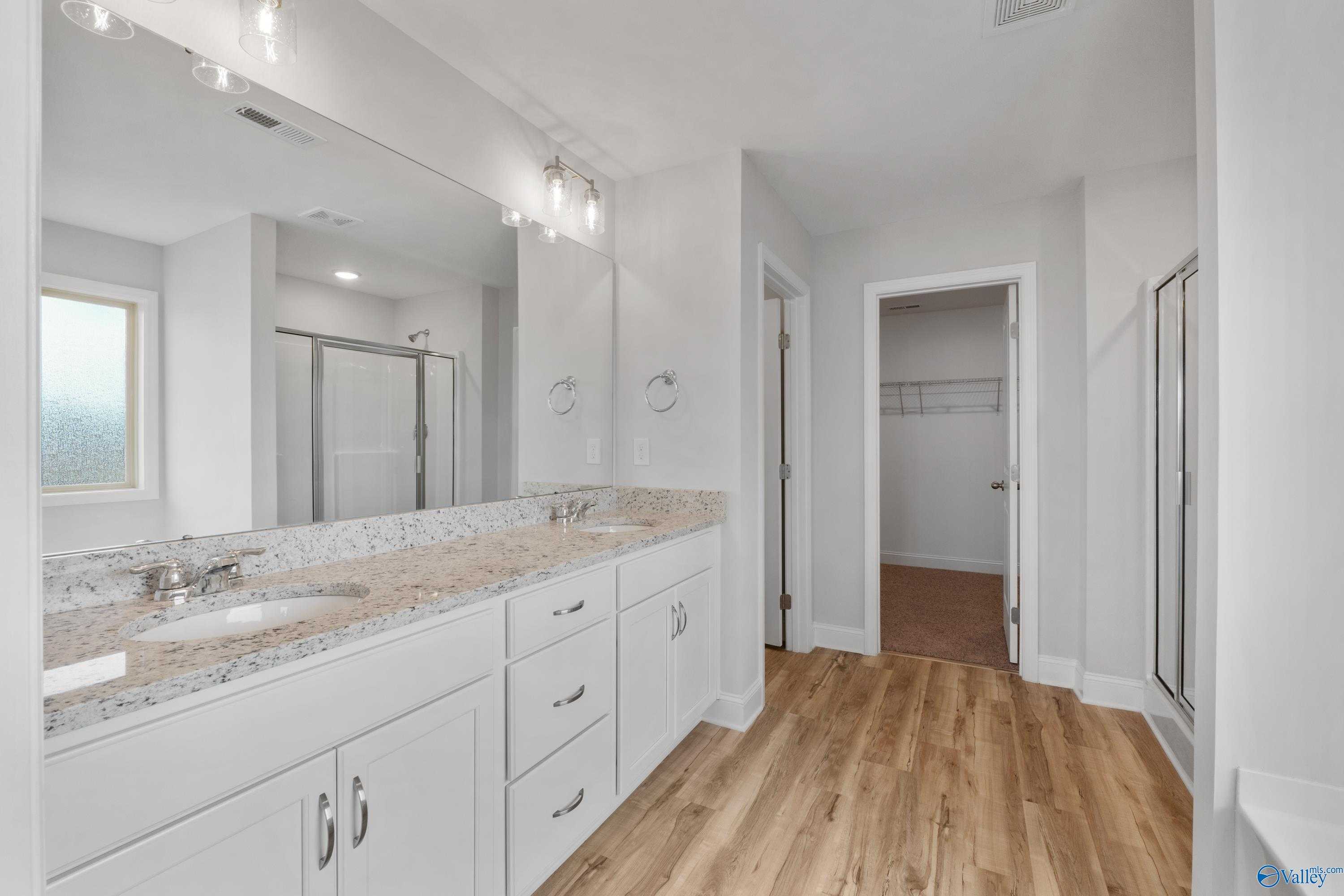 Elegant master bathroom with double granite vanity, frameless glass shower, and walk-in closet in Davidson Homes Chelsea C, Harvest AL