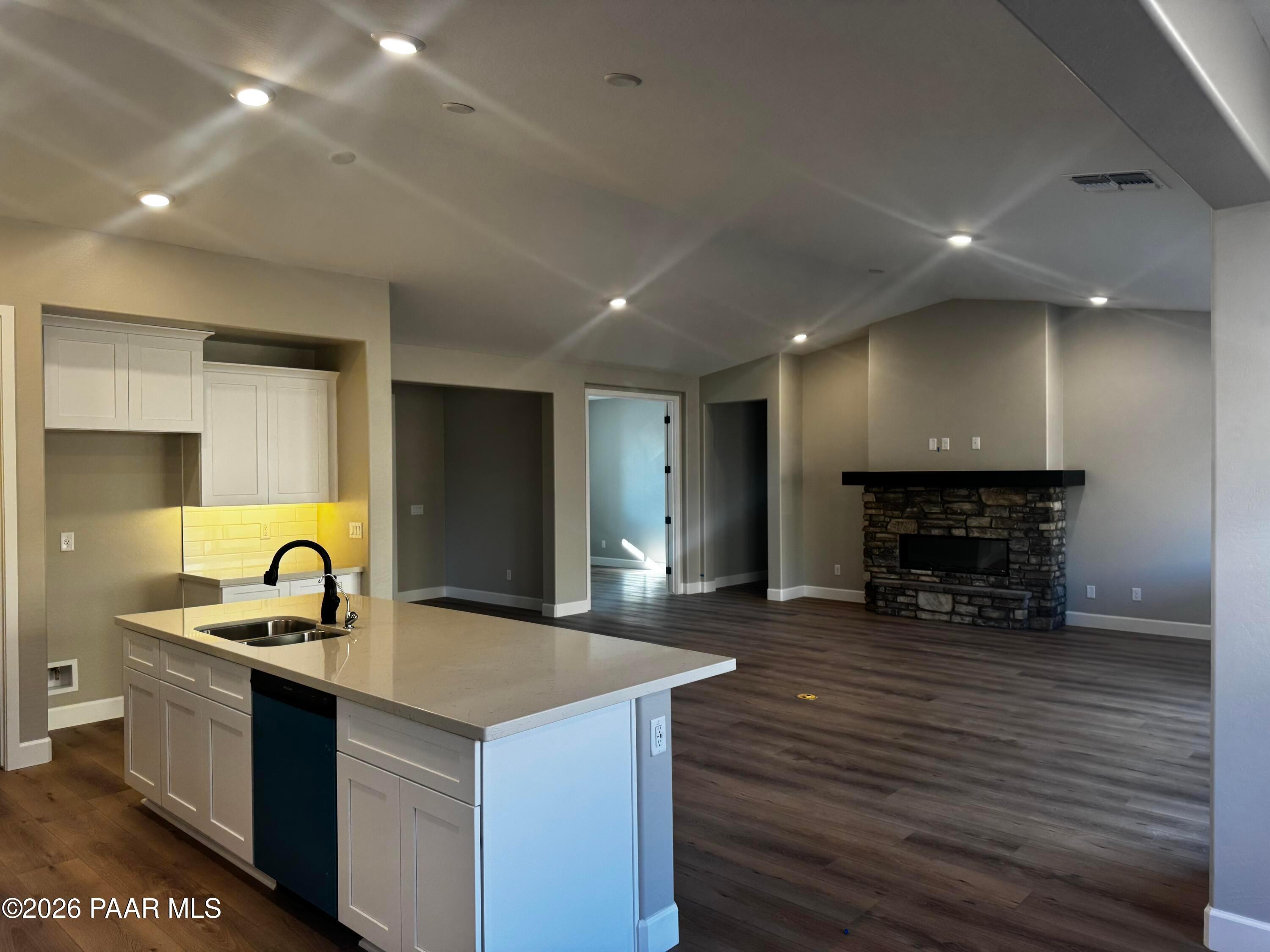 Modern open-concept kitchen with white cabinets, quartz island, and stone fireplace in Evermore Homes The Monarch B, Prescott Valley, AZ