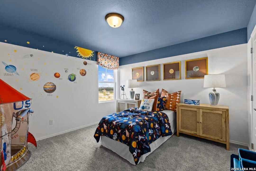 Space-themed kids' bedroom with blue ceiling, planet wall decals, rocket toy, starry bedding in Davidson Homes The Douglas C, Converse, Texas