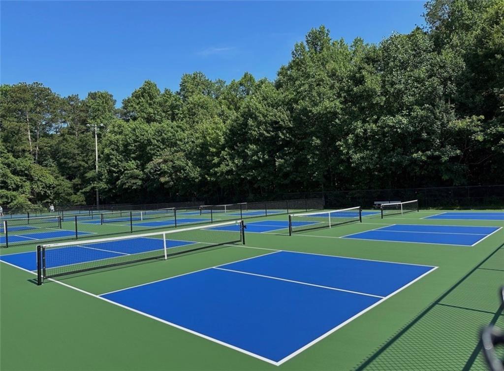 Four blue pickleball courts with nets and fences amid lush trees in Cedar Farms, Winder, Georgia