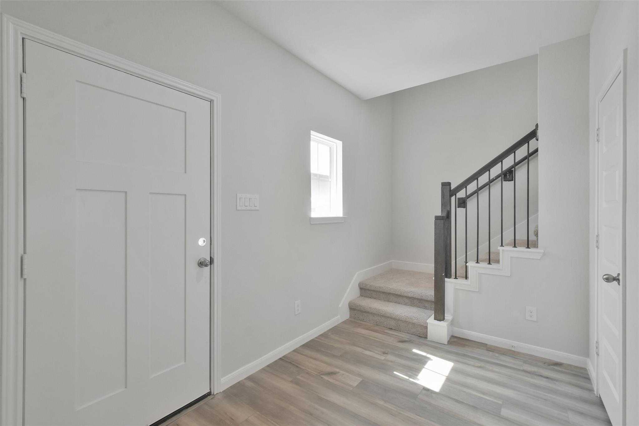 Bright entry foyer with curved staircase, black railing, white doors, and wood floors in Davidson Homes The Tierra A 4-bedroom, Dayton Texas