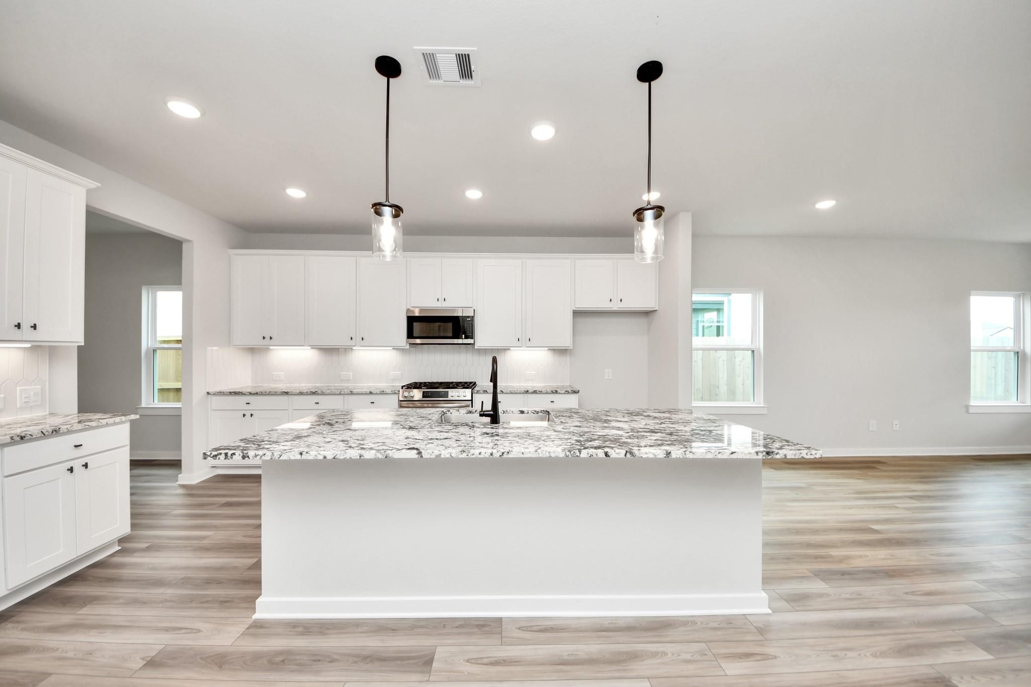 Modern kitchen with white cabinets, granite island, and pendant lighting in The Sorrento E at Sundance Cove, Crosby, Texas.