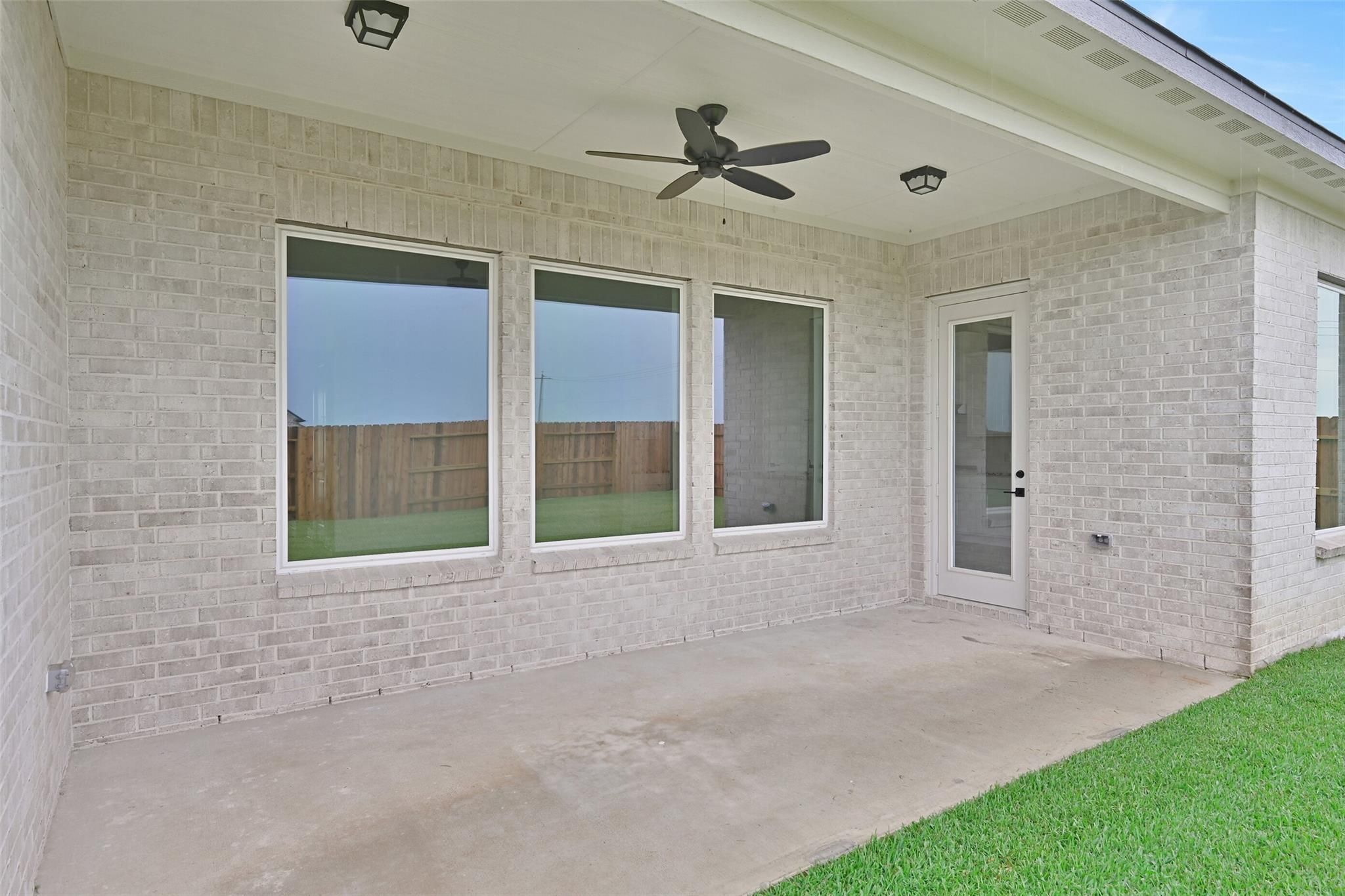 Covered back patio with ceiling fan, large windows, and brick exterior in Davidson Homes The Edward C, Lago Mar, Texas City