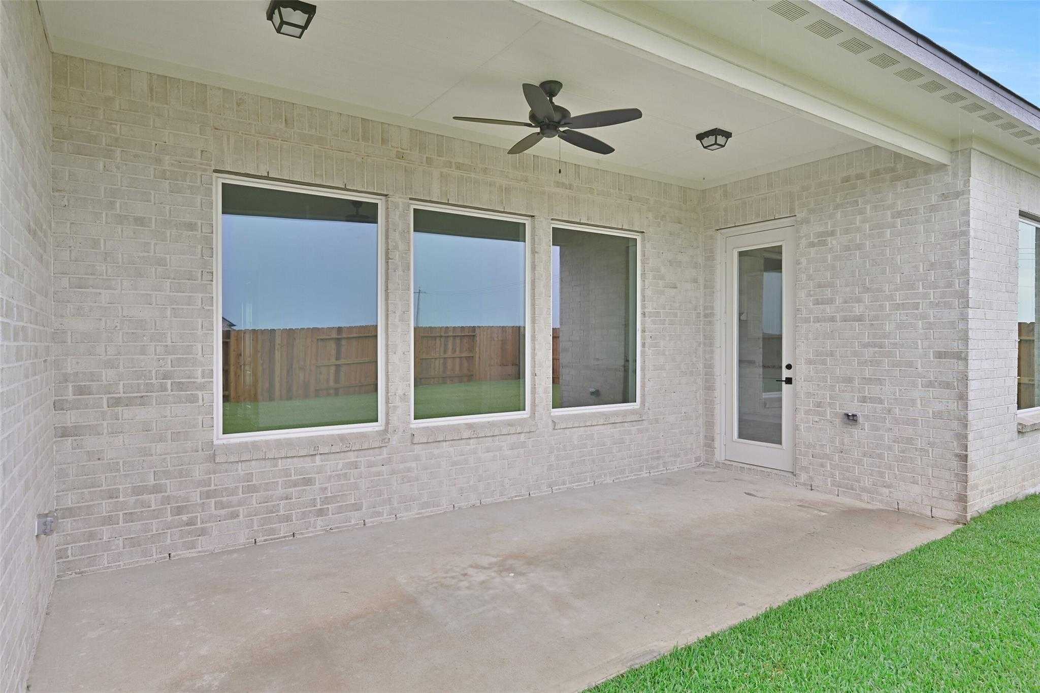 Covered back patio with ceiling fan, large windows, and brick exterior in Davidson Homes The Edward C, Lago Mar, Texas City