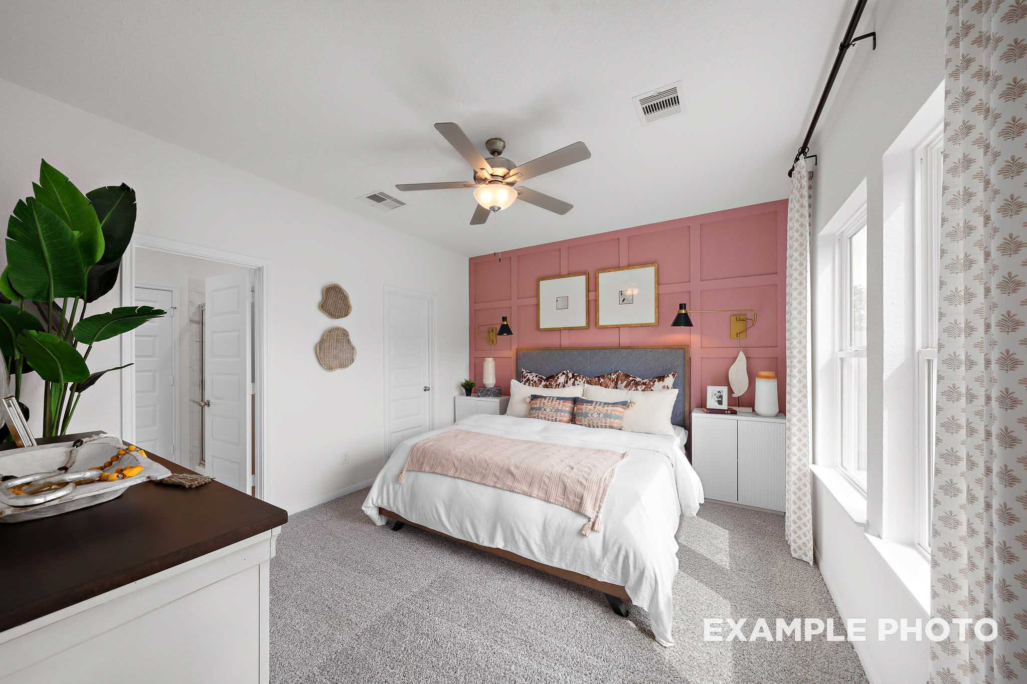 Spacious master bedroom in The Sabine E with pink accent wall, king bed, ceiling fan, and large windows