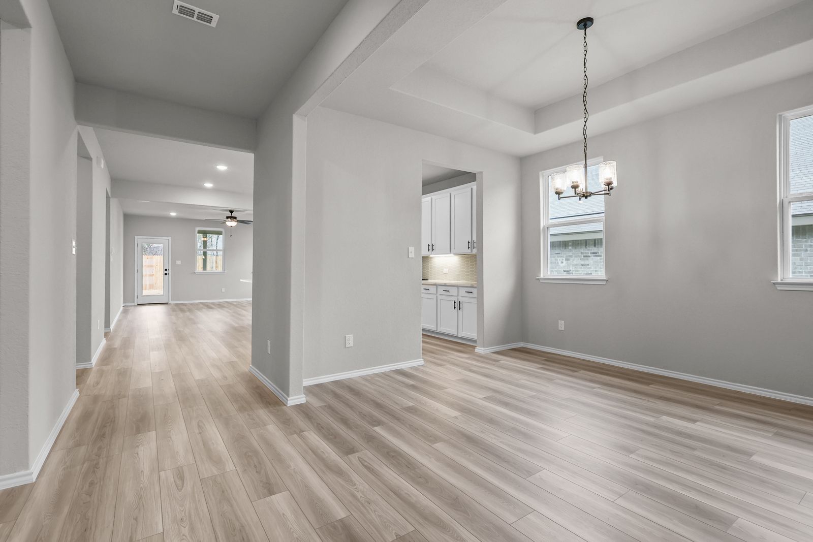 Open-concept dining area and kitchen in The Glenwood featuring light wood-look flooring and a modern tray ceiling.
