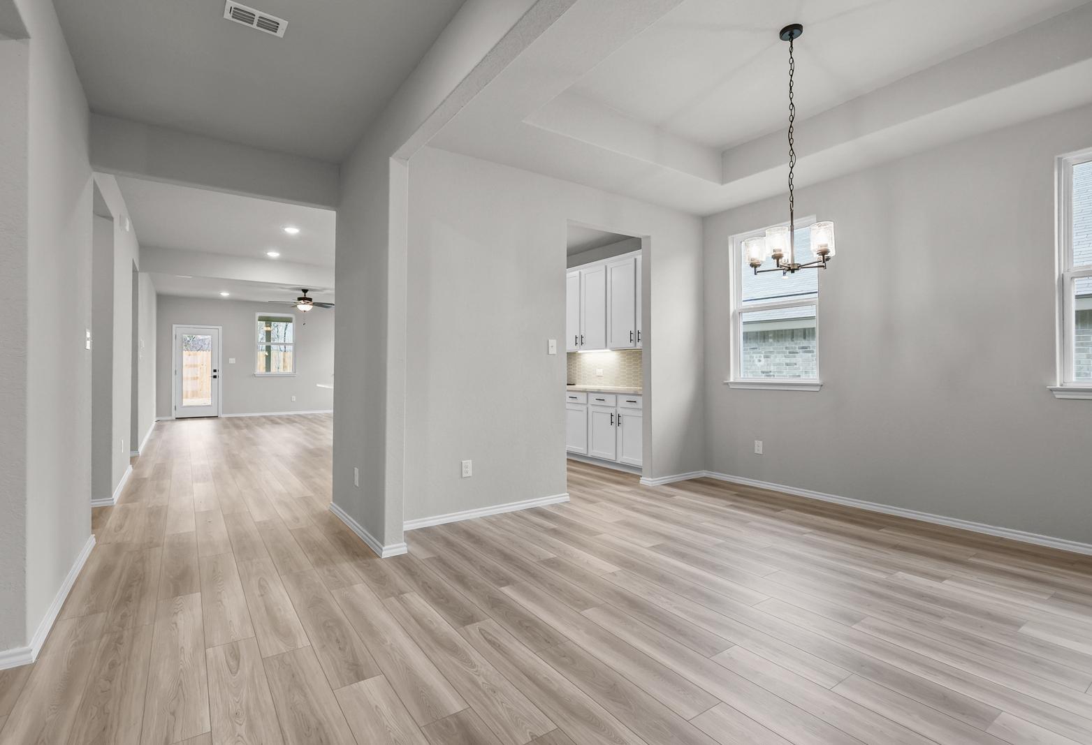 Open-concept dining area and kitchen in The Glenwood D, featuring light wood flooring and modern tray ceiling lighting.