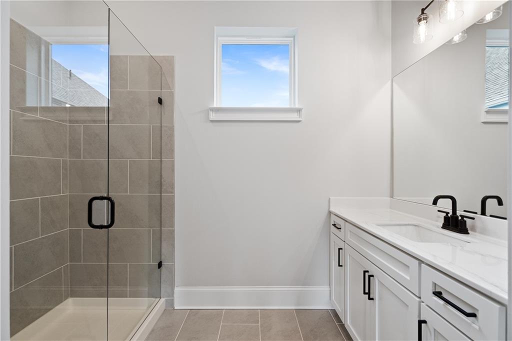Modern master bathroom featuring frameless glass shower, gray tile, white quartz vanity, black faucets in Davidson Homes The Seaside B, Woodstock, GA