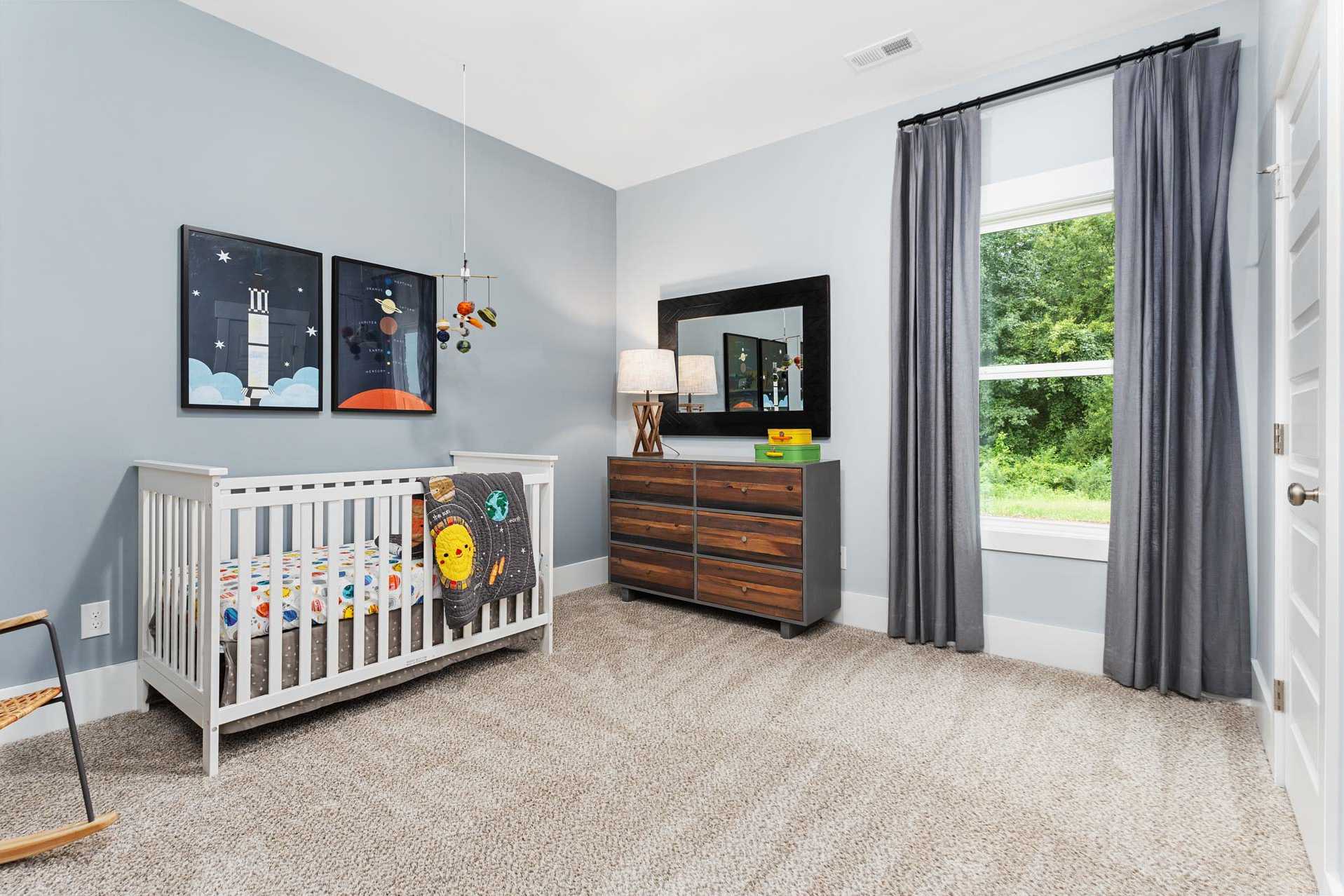 Cozy space-themed nursery at The Meadows in Athens Alabama with light blue walls crib dresser and window view