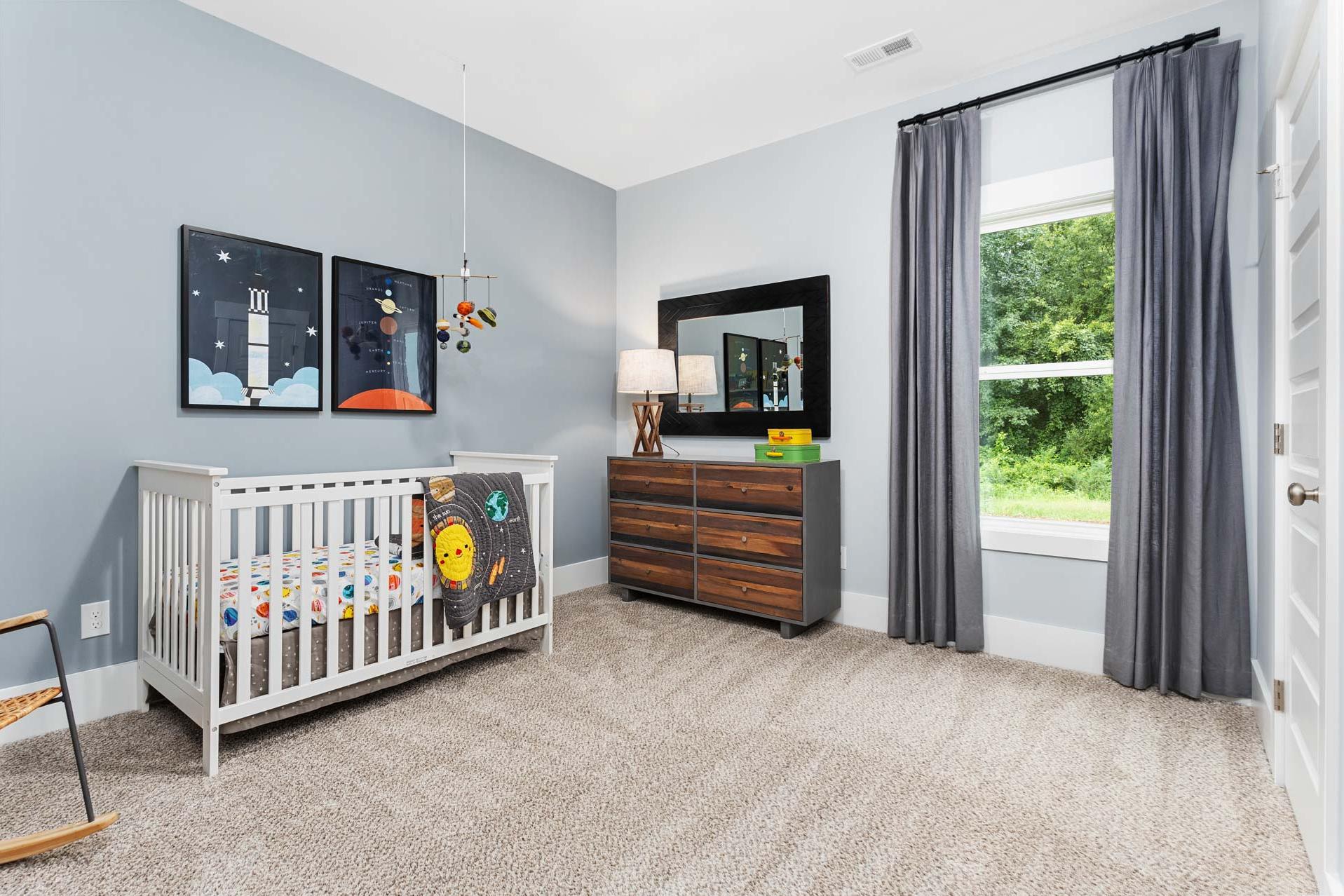 Cozy space-themed nursery at The Meadows in Athens Alabama with light blue walls crib dresser and window view