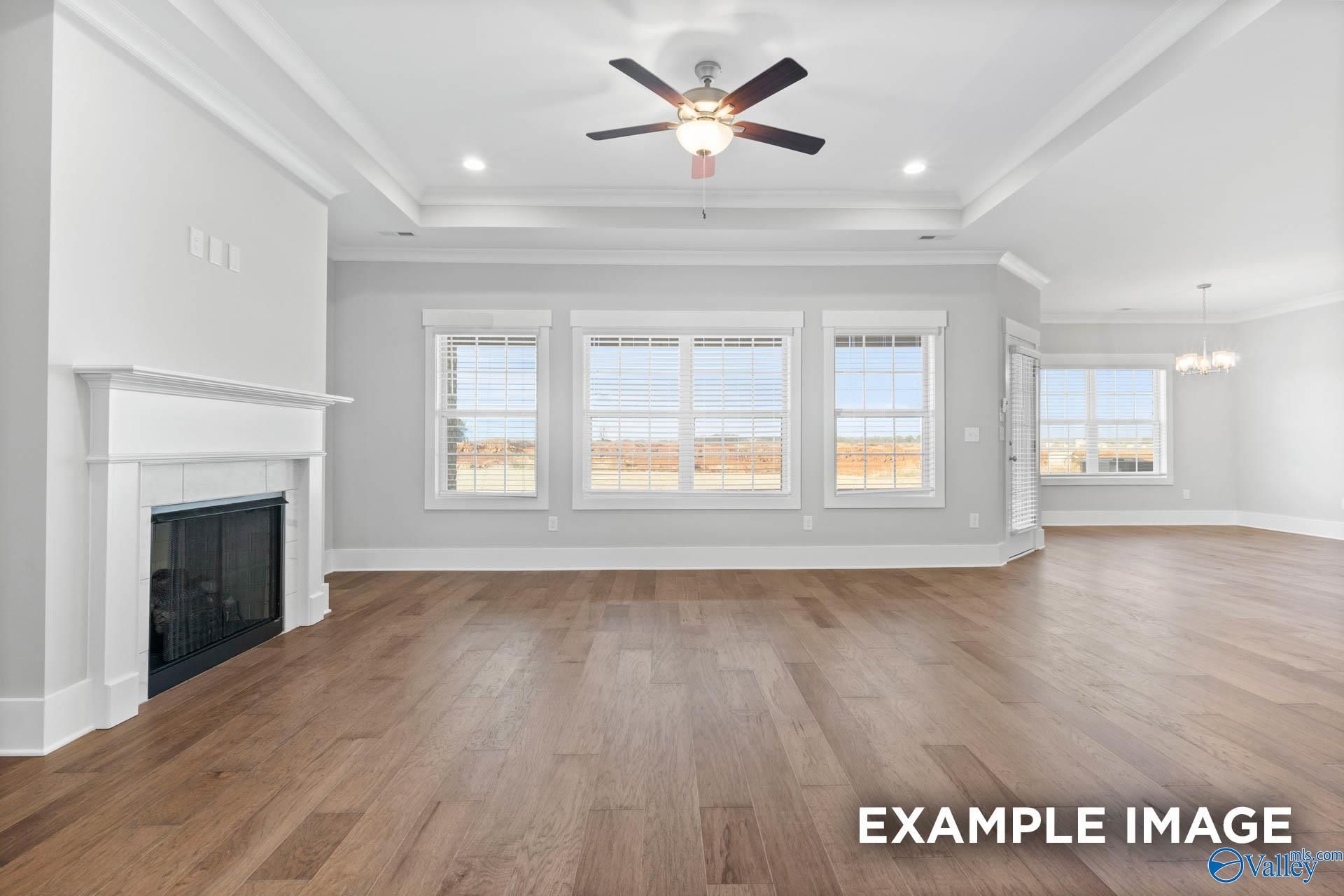 Bright living room with gas fireplace, large triple windows, ceiling fan, and hardwood floors in Davidson Homes The Rockford, Meridianville, Alabama