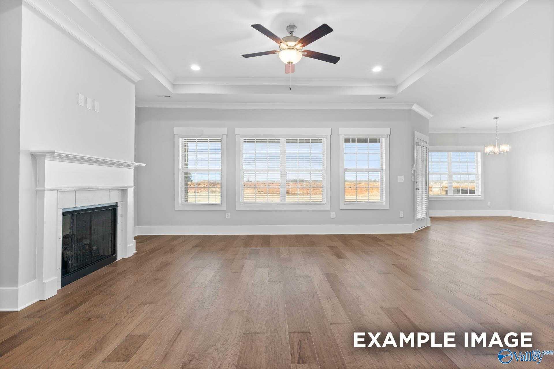 Bright living room with gas fireplace, large triple windows, ceiling fan, and hardwood floors in Davidson Homes The Rockford, Meridianville, Alabama