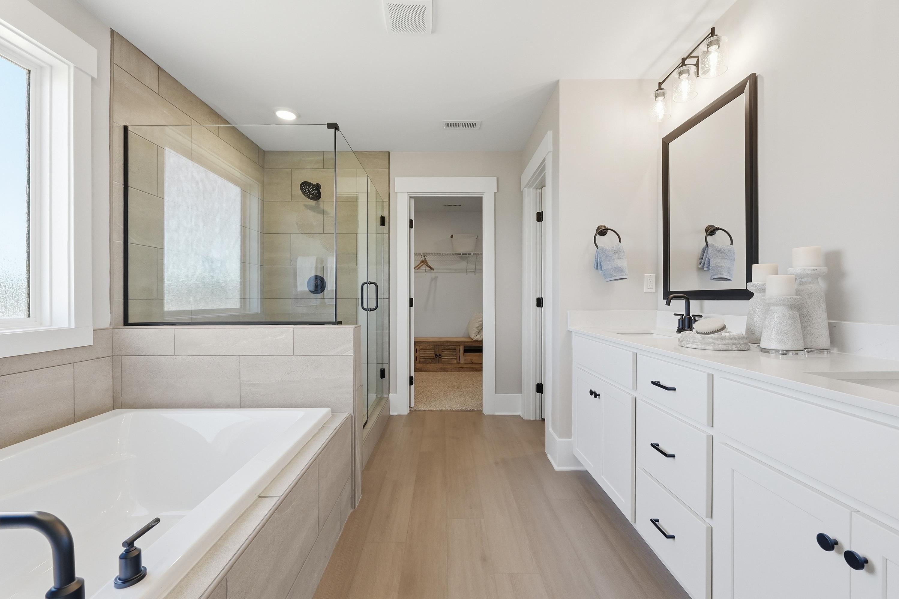 Spacious primary bathroom at Berry Cove in New Market Alabama featuring glass shower, soaking tub, double white vanity, and hardwood floors