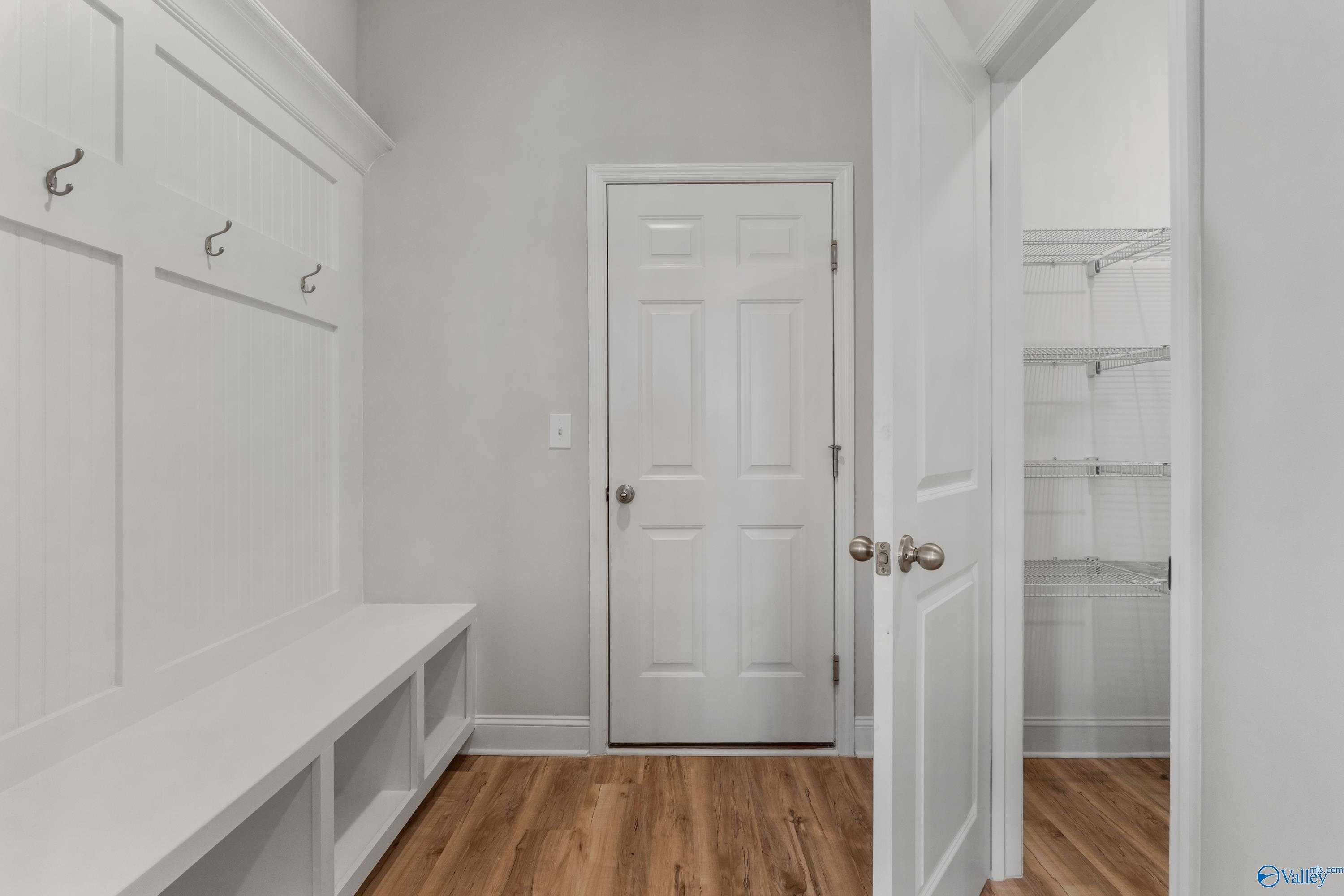 Functional mudroom with white paneled walls, built-in bench, coat hooks, and adjacent open pantry shelving in Davidson Homes Chelsea C, Harvest AL