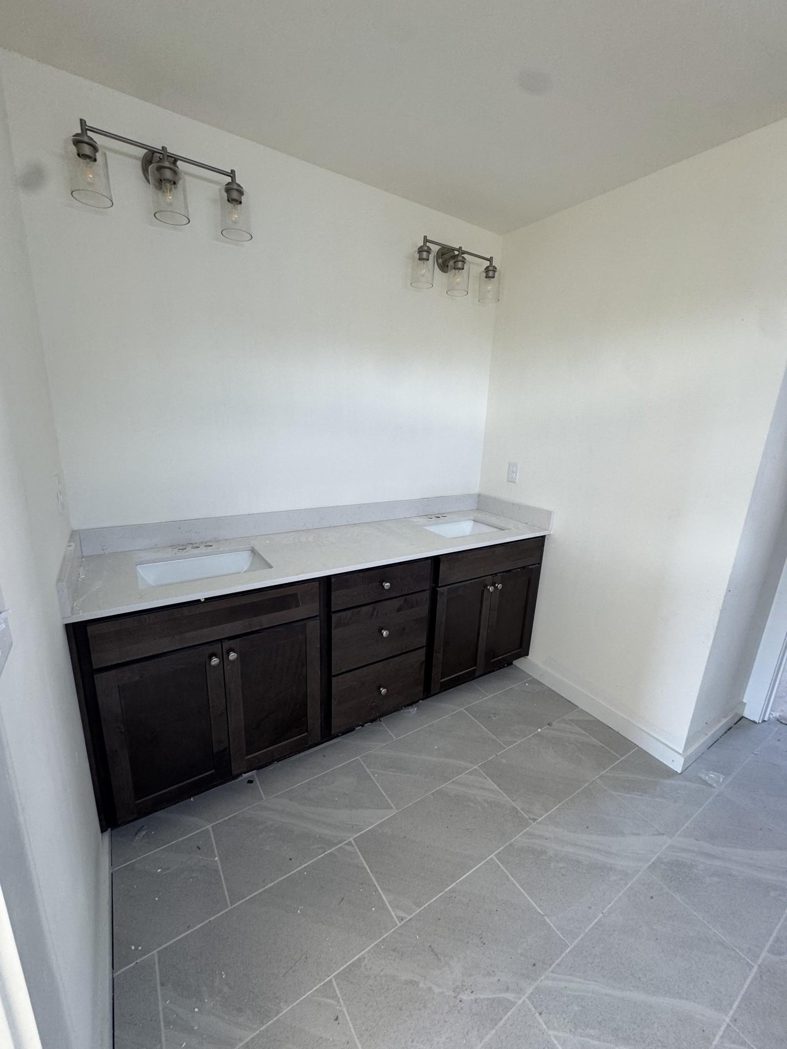 Modern double vanity bathroom with dark cabinets, white quartz counters, dual sinks, and gray tile floor in Davidson Homes The Willow C, Gallatin, TN