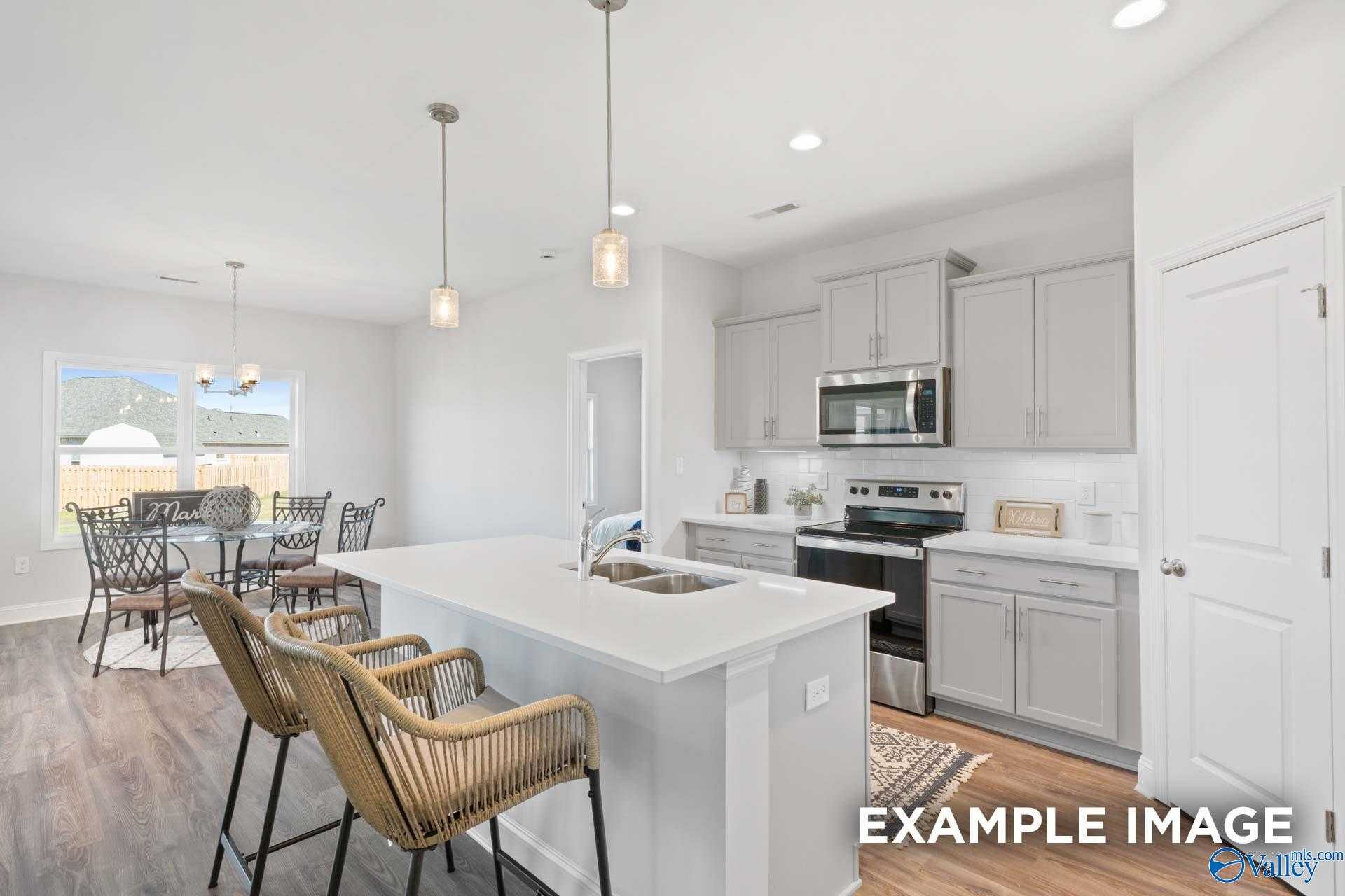 Modern open-concept kitchen with white shaker cabinets, stainless appliances, island sink, and wicker bar stools in The Franklin C, Meridianville, AL