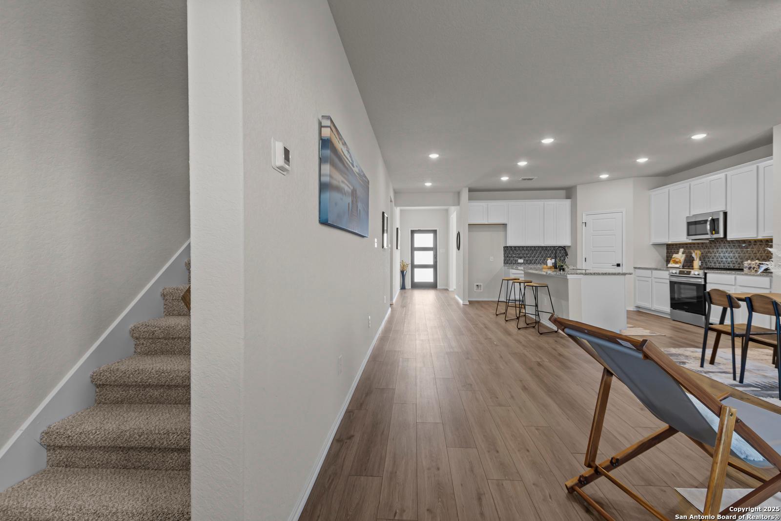 Spacious hallway with carpeted staircase and open white kitchen island in Davidson Homes The Douglas C, Seguin, Texas