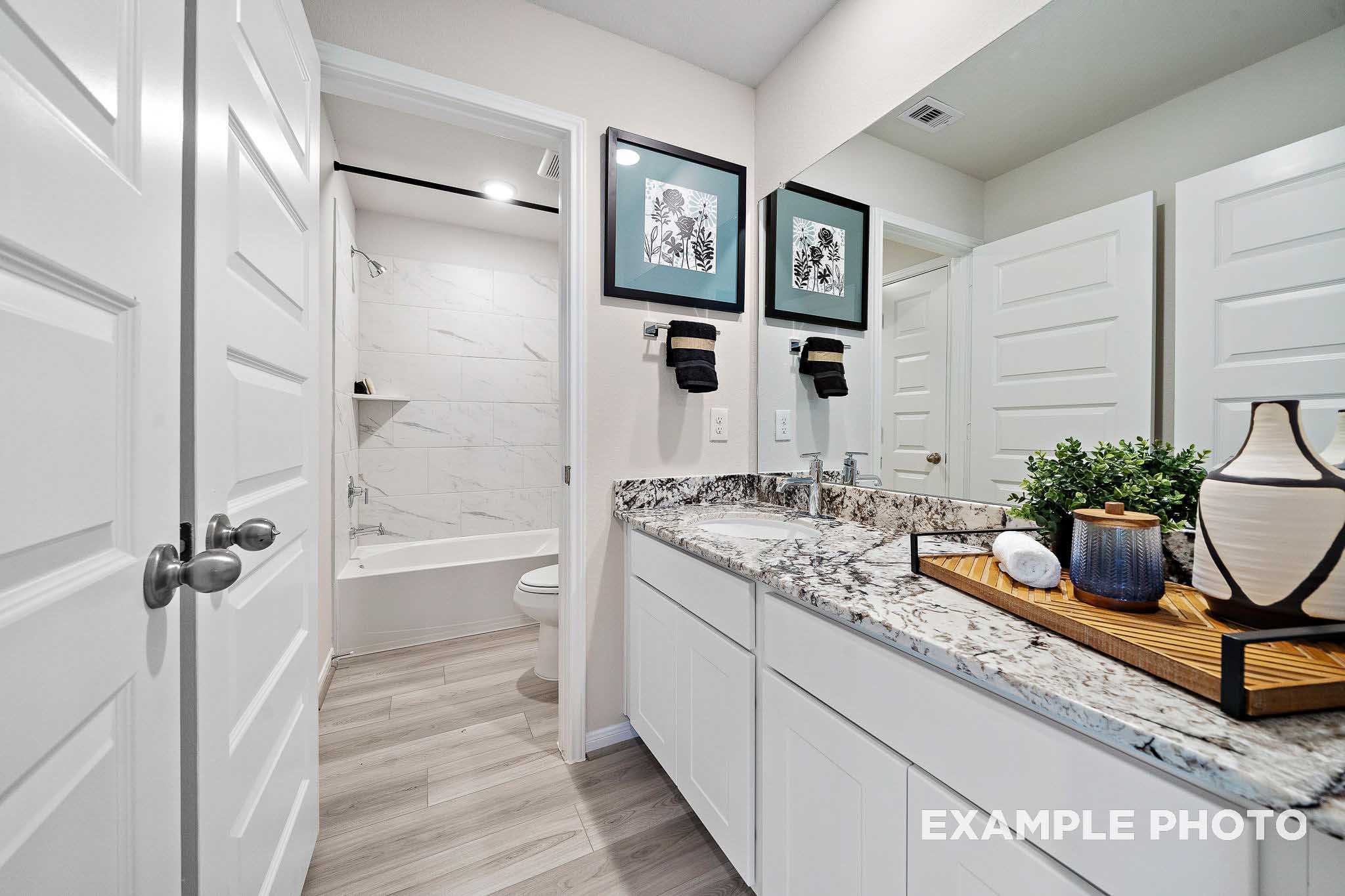 Spacious master bathroom in The San Marcos B featuring double vanity, quartz countertop, soaking tub, and tiled walk-in shower