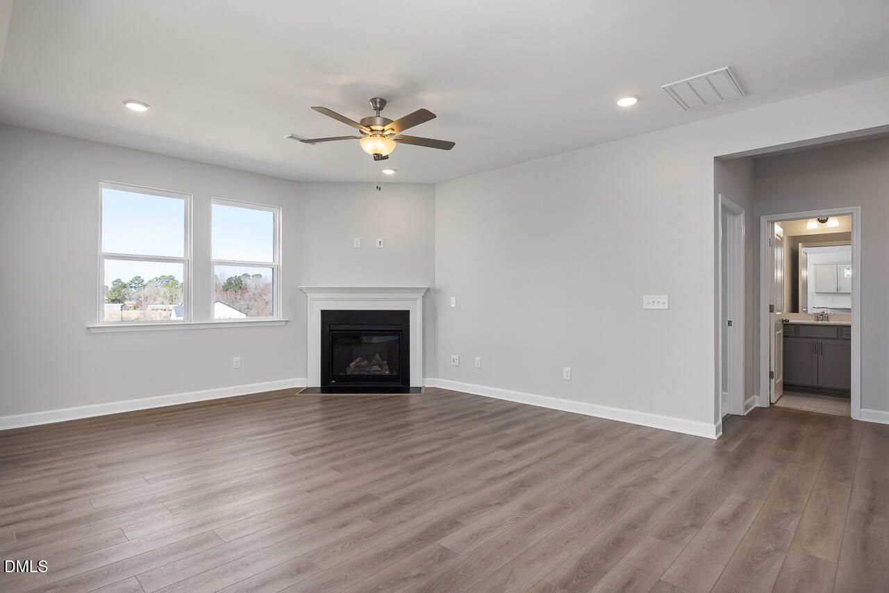 Spacious living room with gas fireplace, ceiling fan, large windows, and adjacent bath in Davidson Homes The Willow G, Angier NC