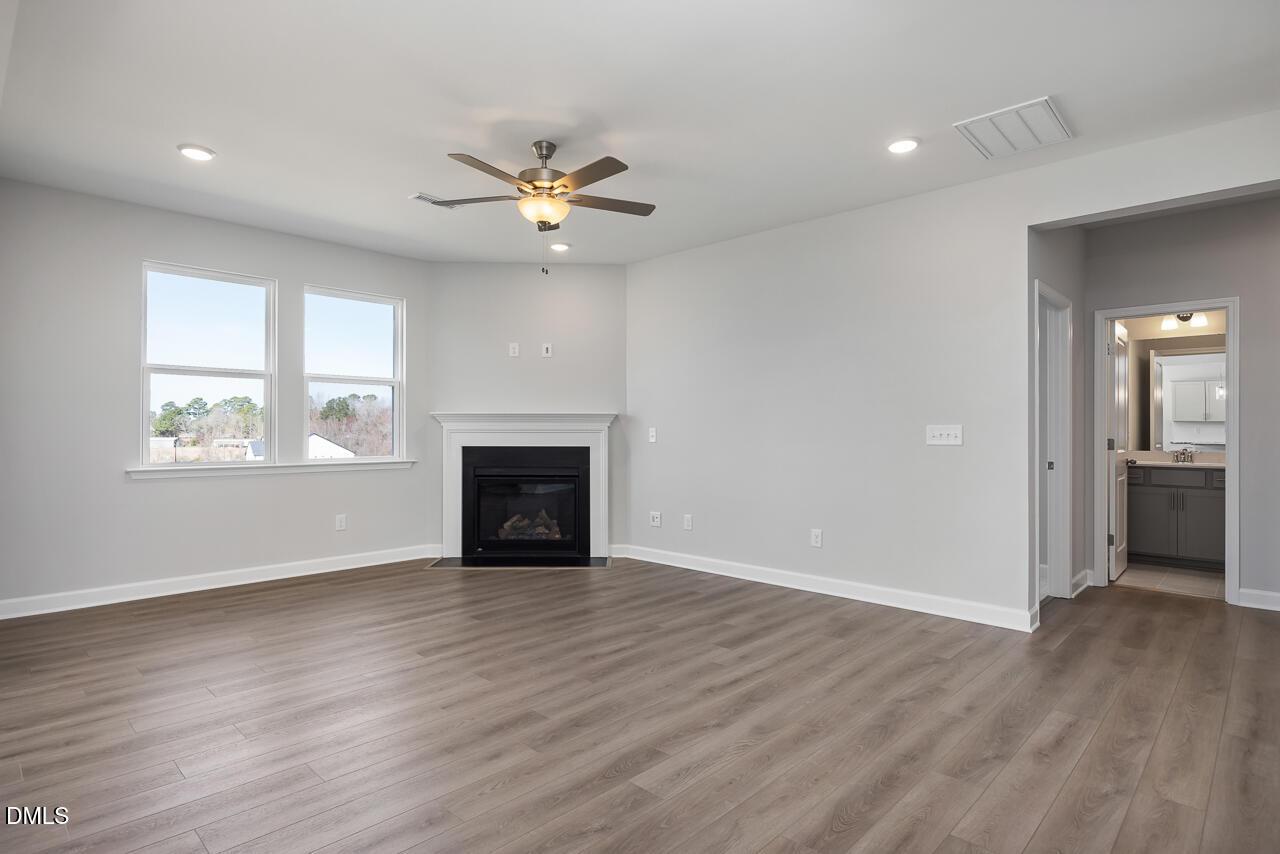 Spacious living room with gas fireplace, ceiling fan, large windows, and adjacent bath in Davidson Homes The Willow G, Angier NC