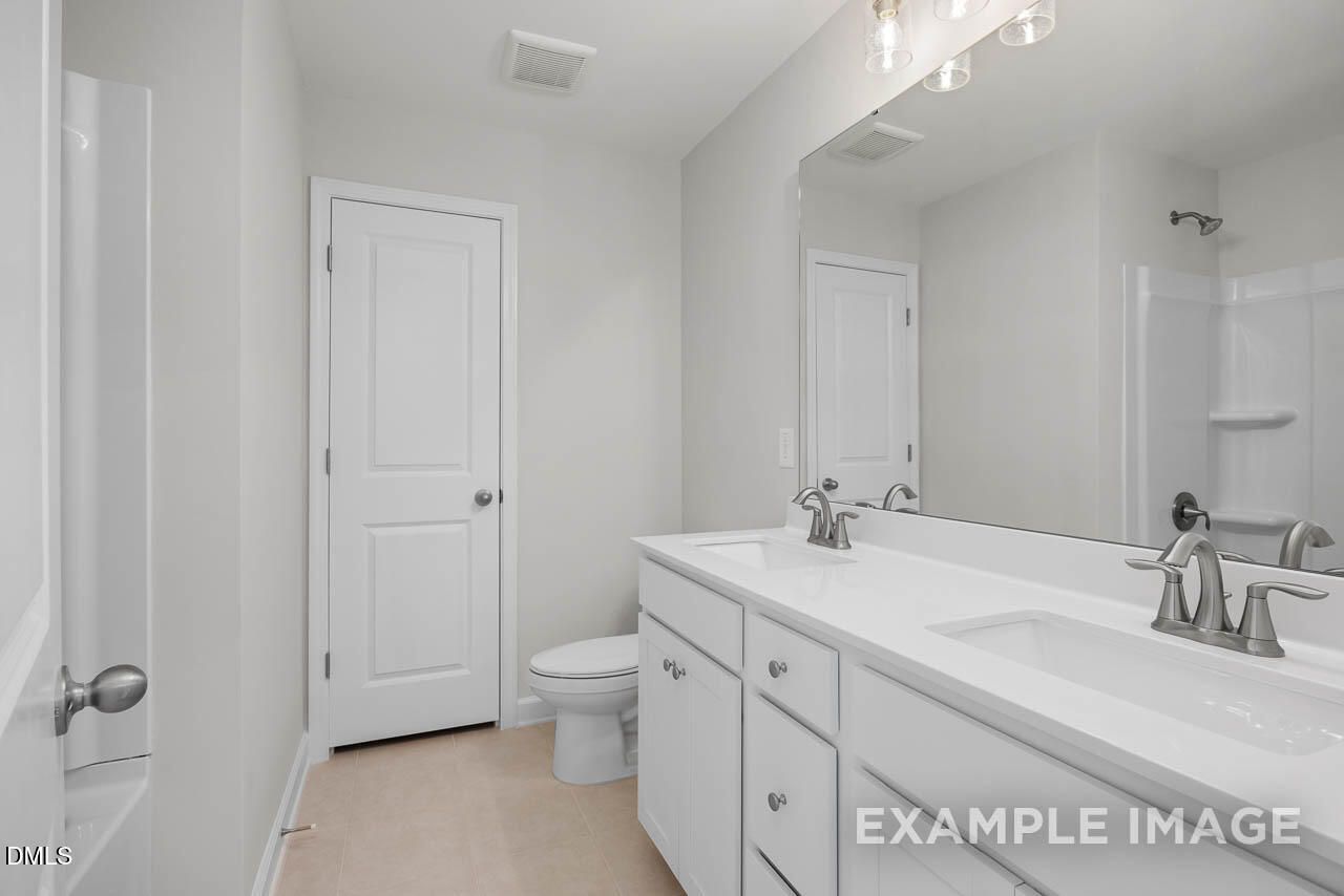 Bright modern bathroom with double vanity, large mirror, and walk-in shower in Davidson Homes The Adalynn A, Lillington, NC