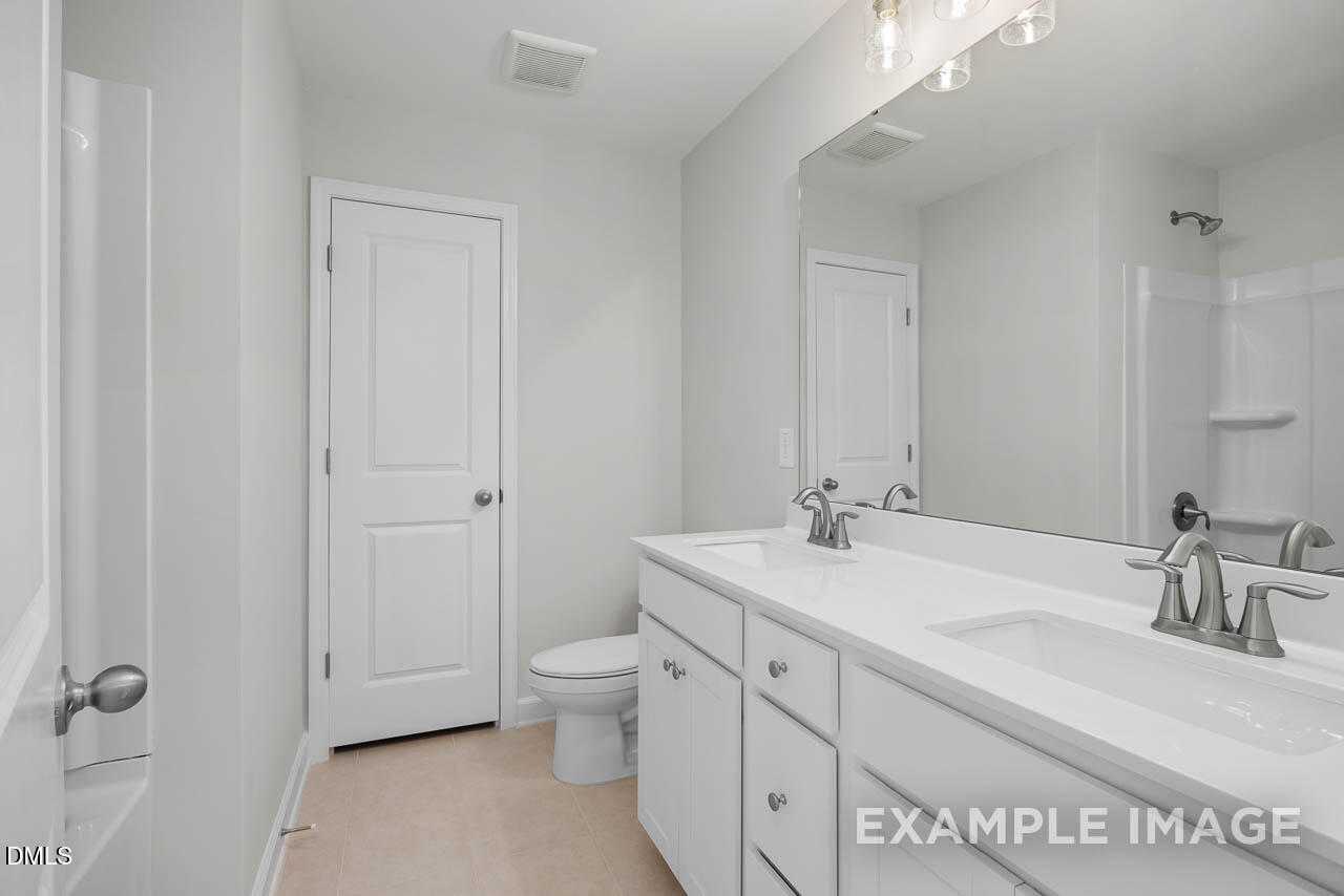 Bright modern bathroom with double vanity, large mirror, and walk-in shower in Davidson Homes The Adalynn A, Lillington, NC