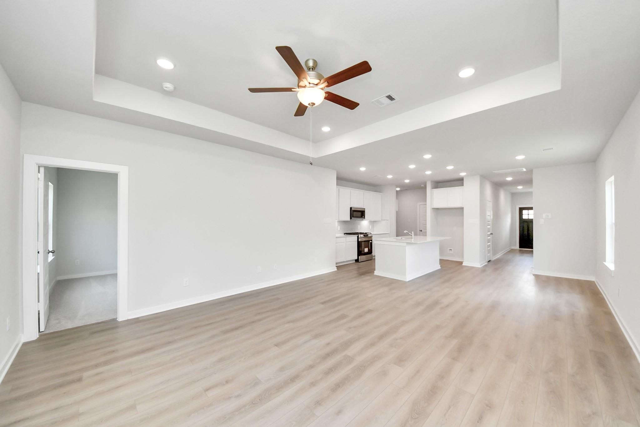 Open-concept living room with tray ceiling and kitchen in The Blanco E floor plan at Caney Creek Place, Conroe, Texas.