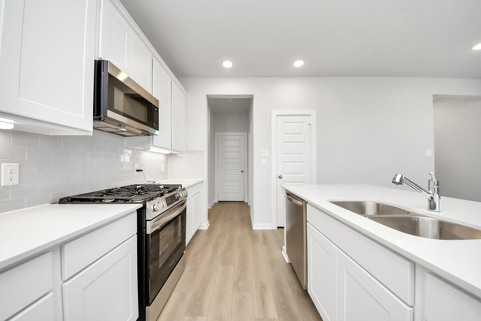 Modern kitchen with white cabinets, stainless steel appliances, and center island in The Costa A floor plan at Emberly.