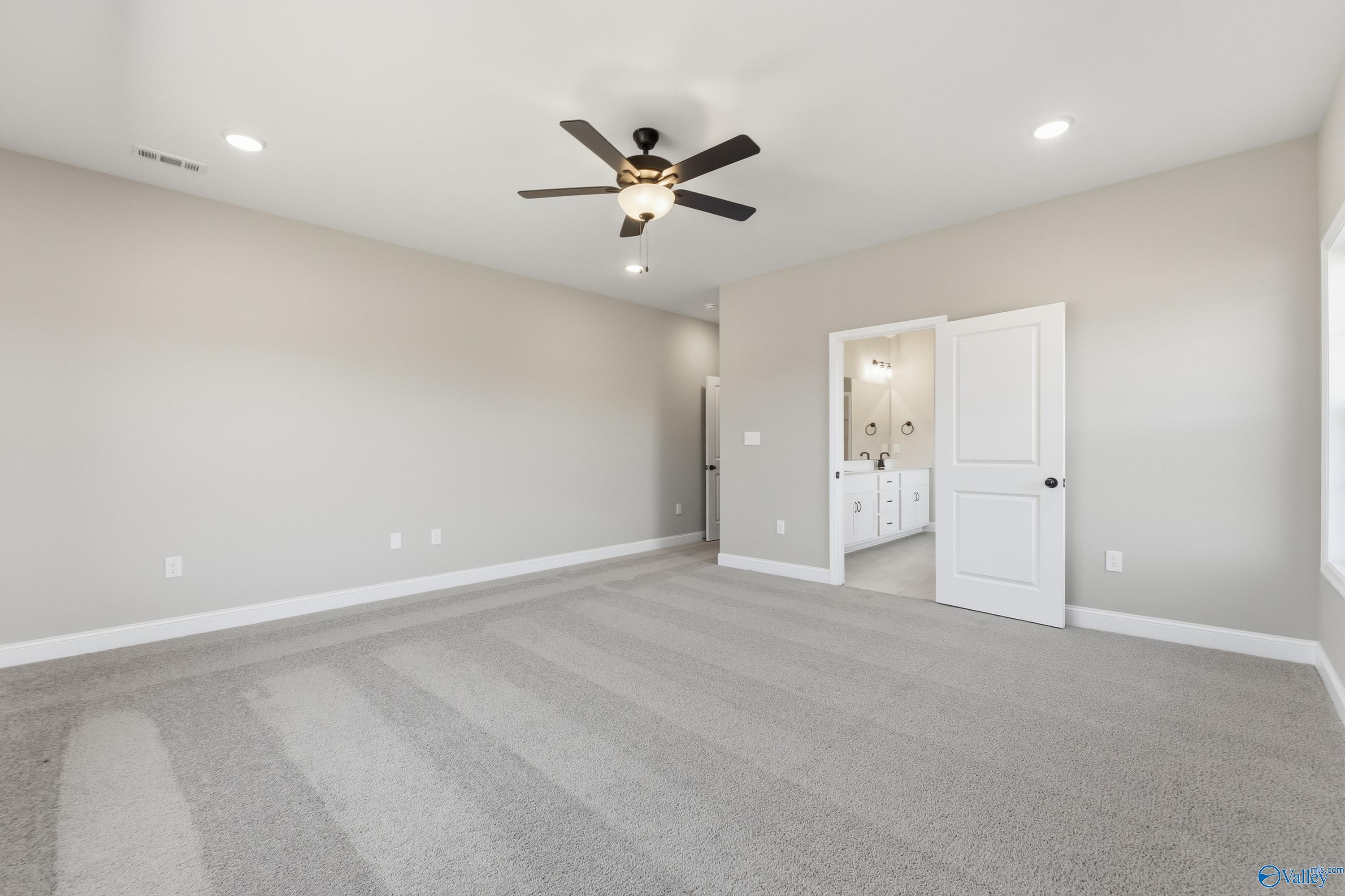Spacious master bedroom with ceiling fan, beige walls, gray carpet, and en-suite bathroom in Davidson Homes The Finleigh, Meridianville, Alabama