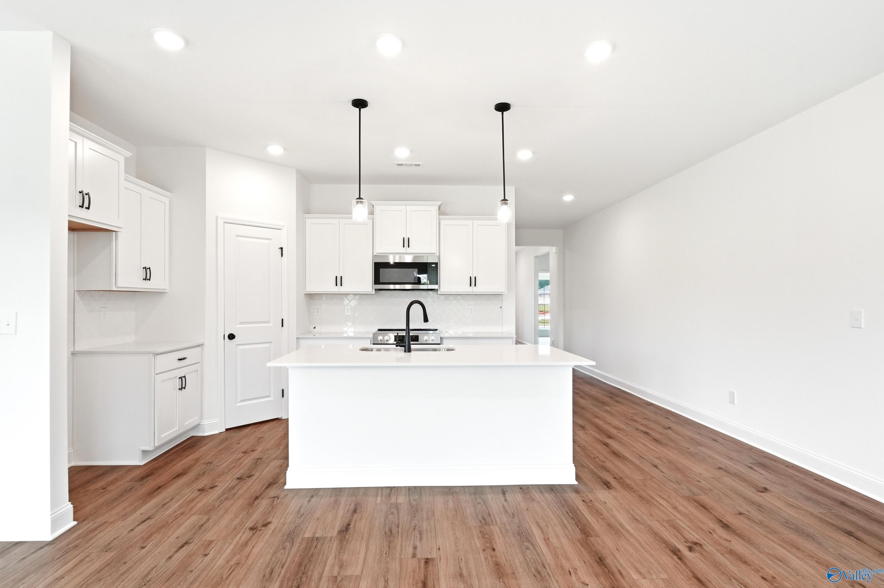 Modern kitchen with white cabinets, island, and wood floors in The Daphne C floor plan by Davidson Homes in Toney, Alabama.