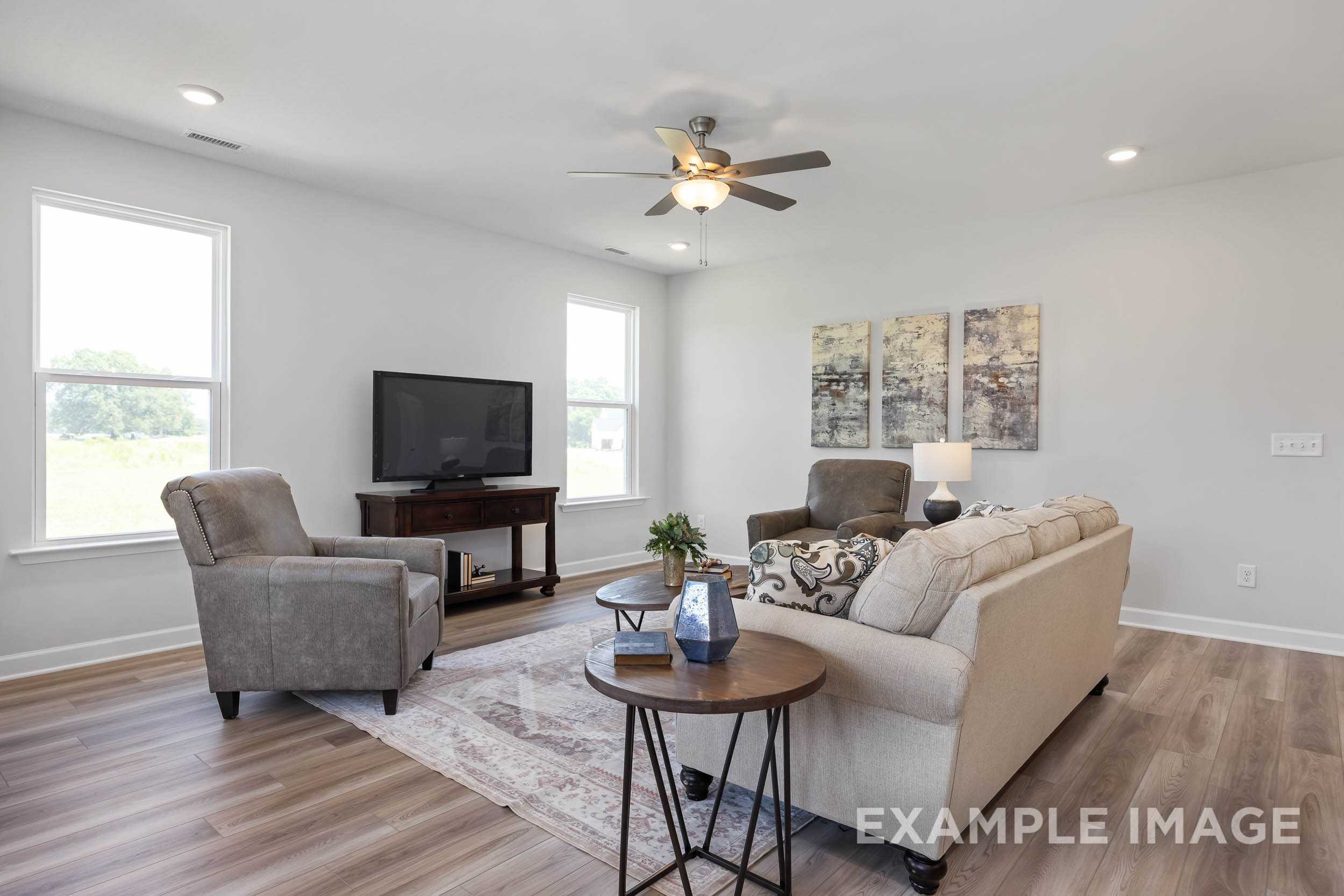 Cozy living room in The Daphne C Davidson Homes design featuring beige sofa, armchairs, TV console, abstract art, ceiling fan, and hardwood floors