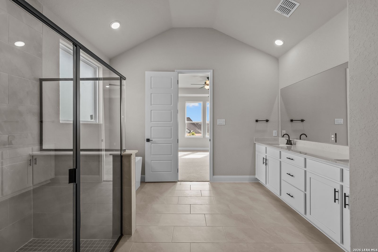 Primary bathroom with glass walk-in shower, dual vanity, and vaulted ceiling in Davidson Homes The Foster E, Castroville, Texas