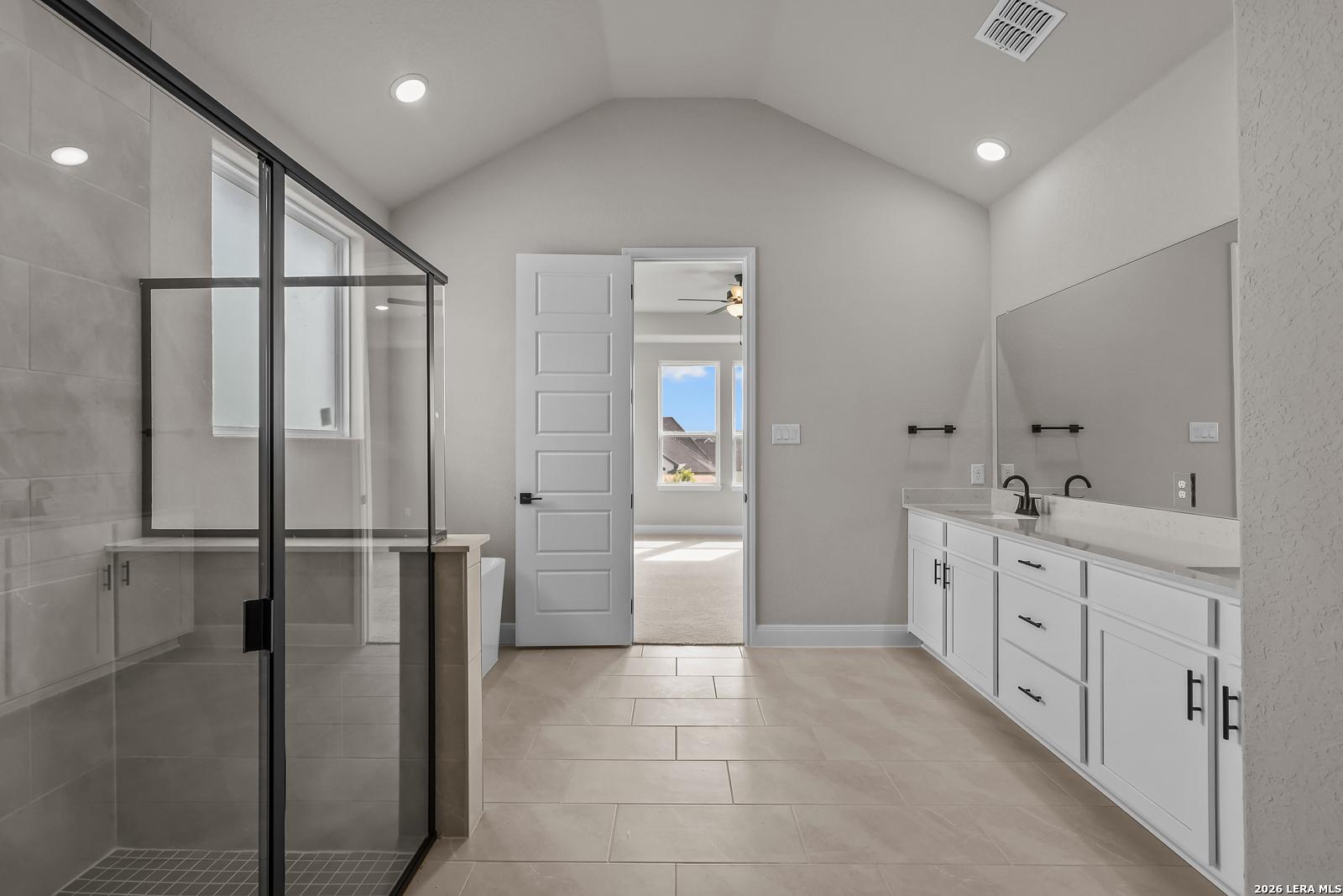 Primary bathroom with glass walk-in shower, dual vanity, and vaulted ceiling in Davidson Homes The Foster E, Castroville, Texas