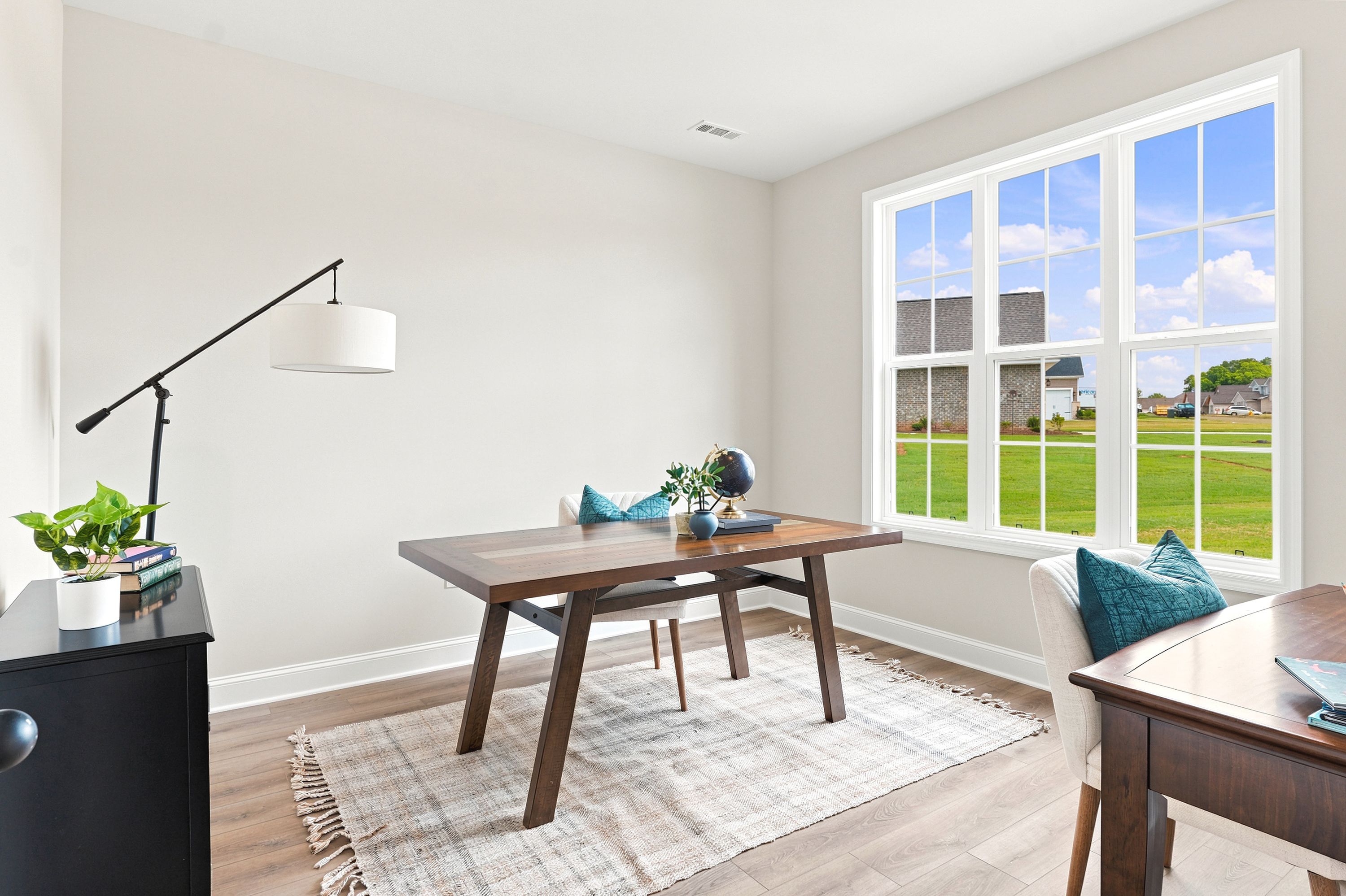 Bright home office at Riverton Preserve in Huntsville, AL with a wood desk, modern floor lamp, and large windows.