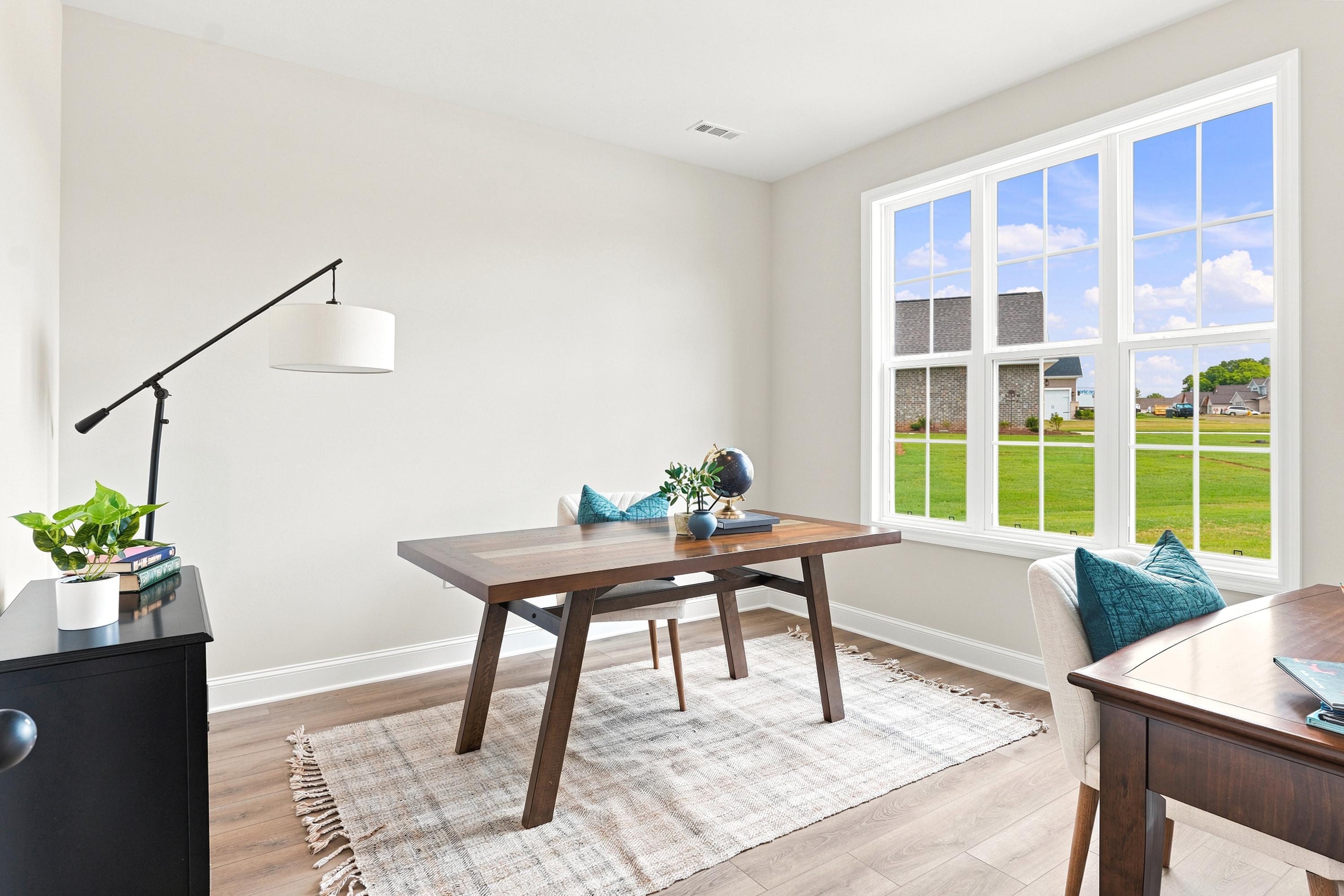 Bright home office at Riverton Preserve in Huntsville, AL with a wood desk, modern floor lamp, and large windows.