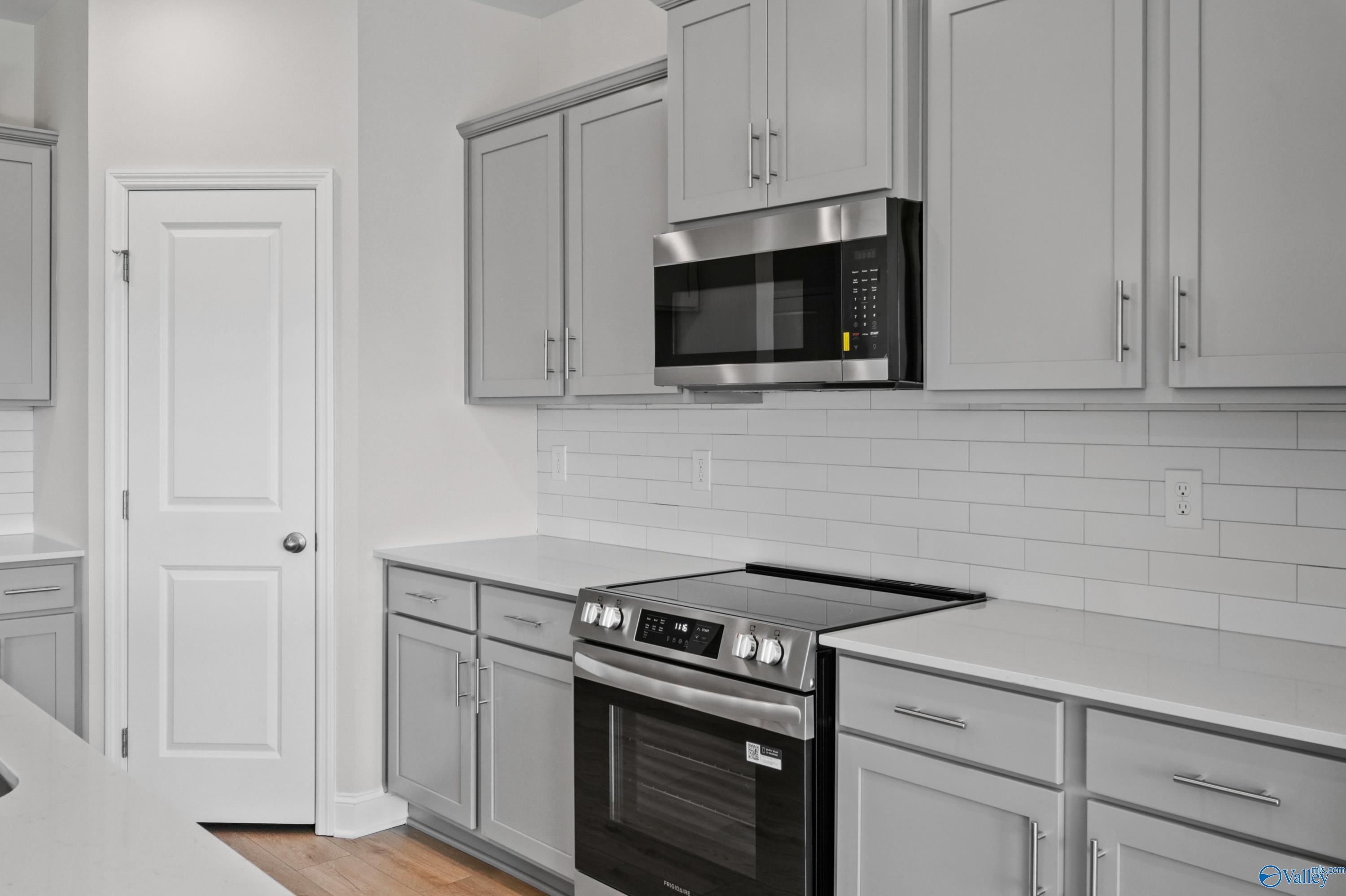 Contemporary kitchen with stainless steel appliances, subway tile backsplash, and light gray cabinets in The Everett floor plan, Hazel Green, Alabama
