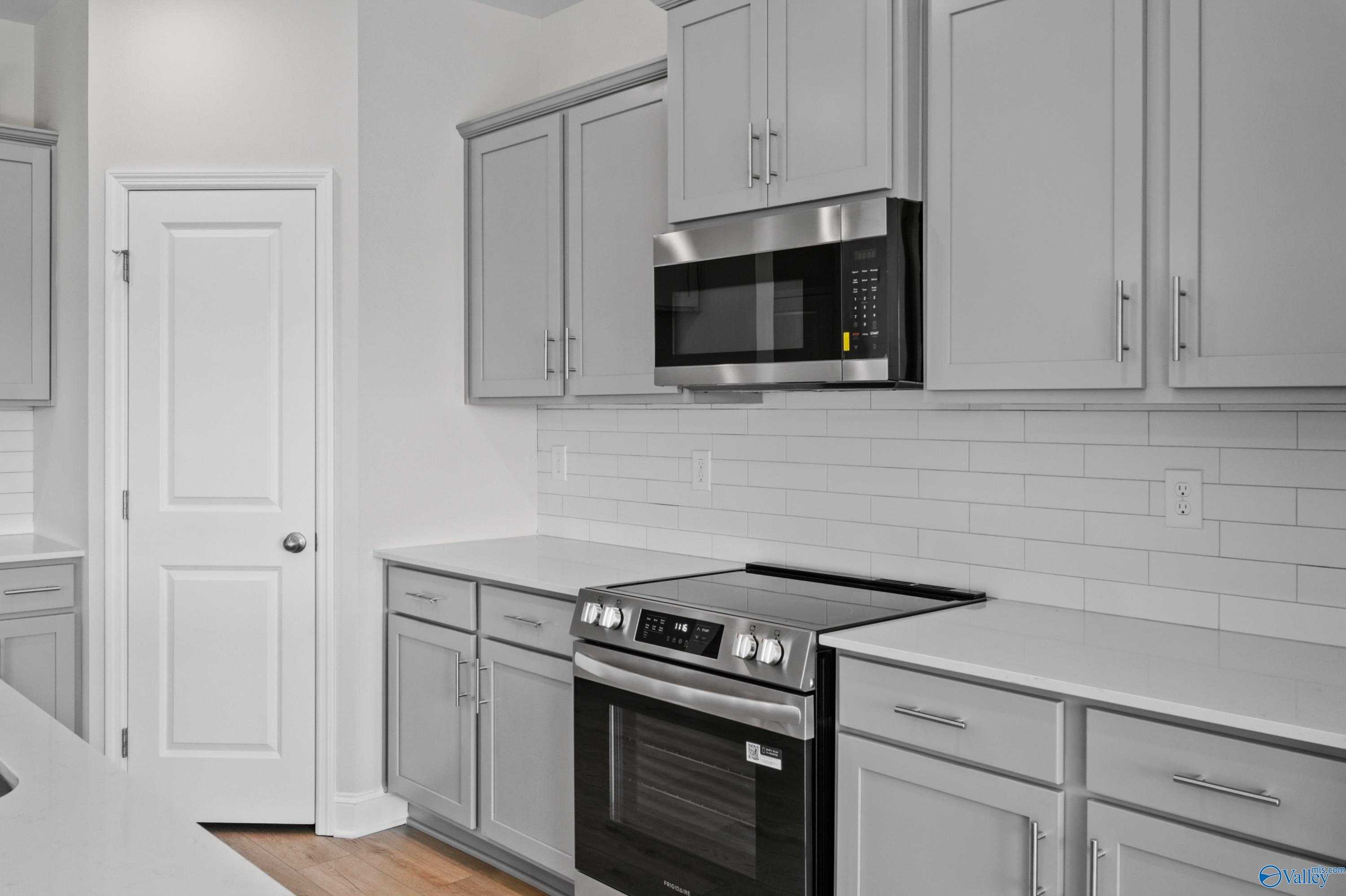 Contemporary kitchen with stainless steel appliances, subway tile backsplash, and light gray cabinets in The Everett floor plan, Hazel Green, Alabama
