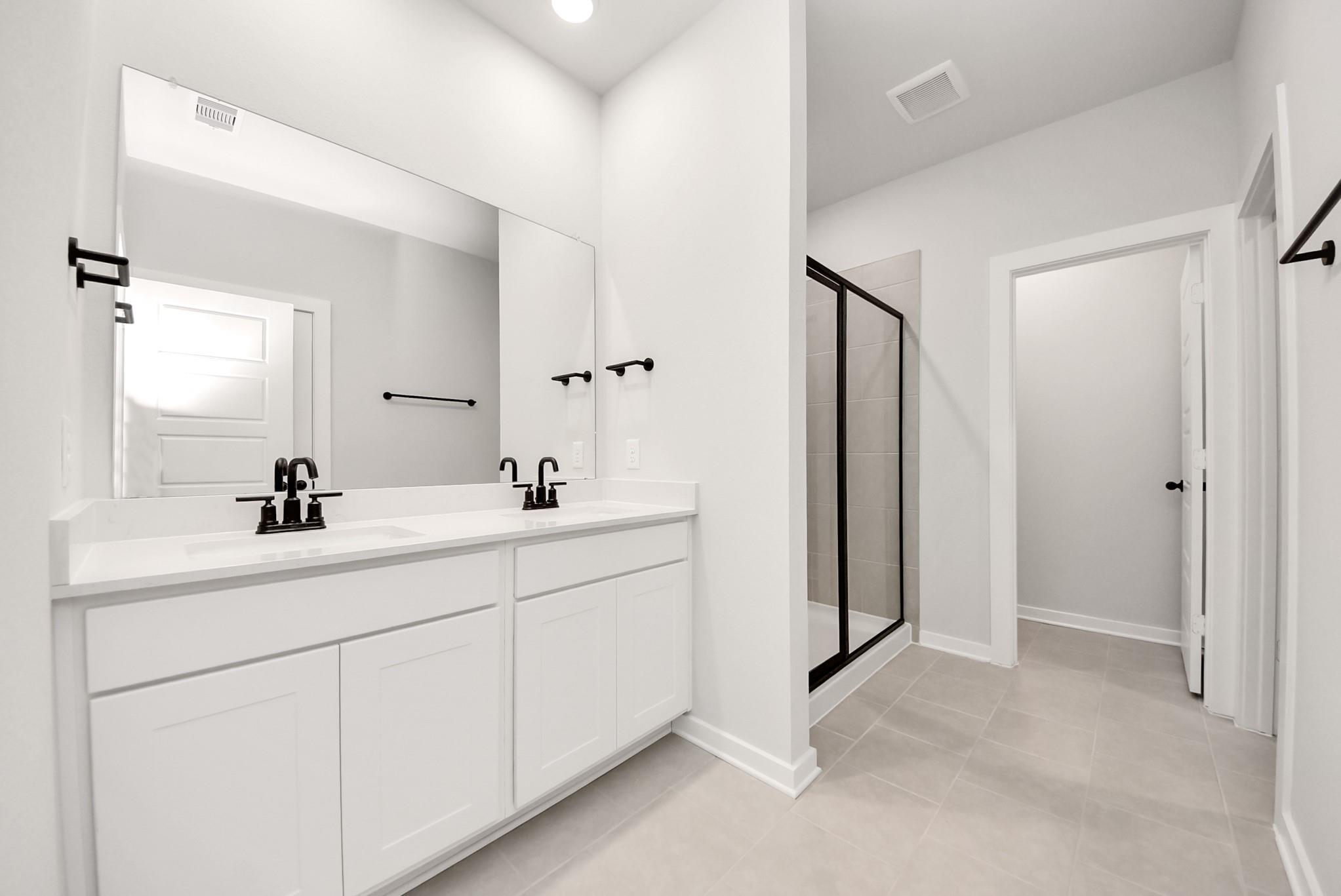 Modern primary bathroom with double vanity, black fixtures, and walk-in shower in The Daphne F plan at Sundance Cove.