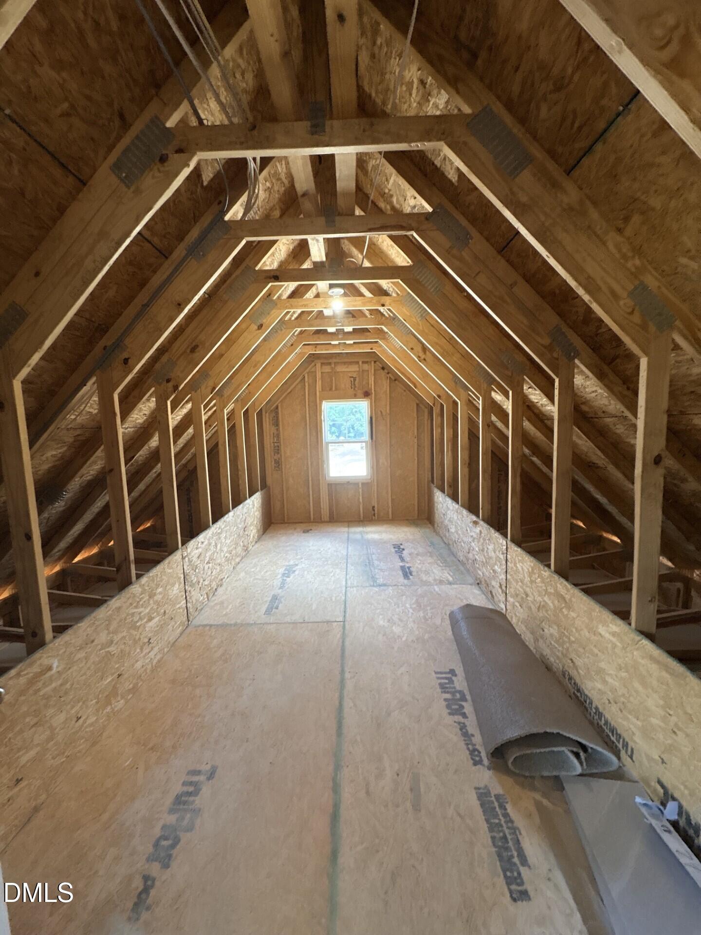 Unfinished attic space with wooden roof trusses and subflooring in The Ash C floor plan at Woodland Crossing, Zebulon, NC.