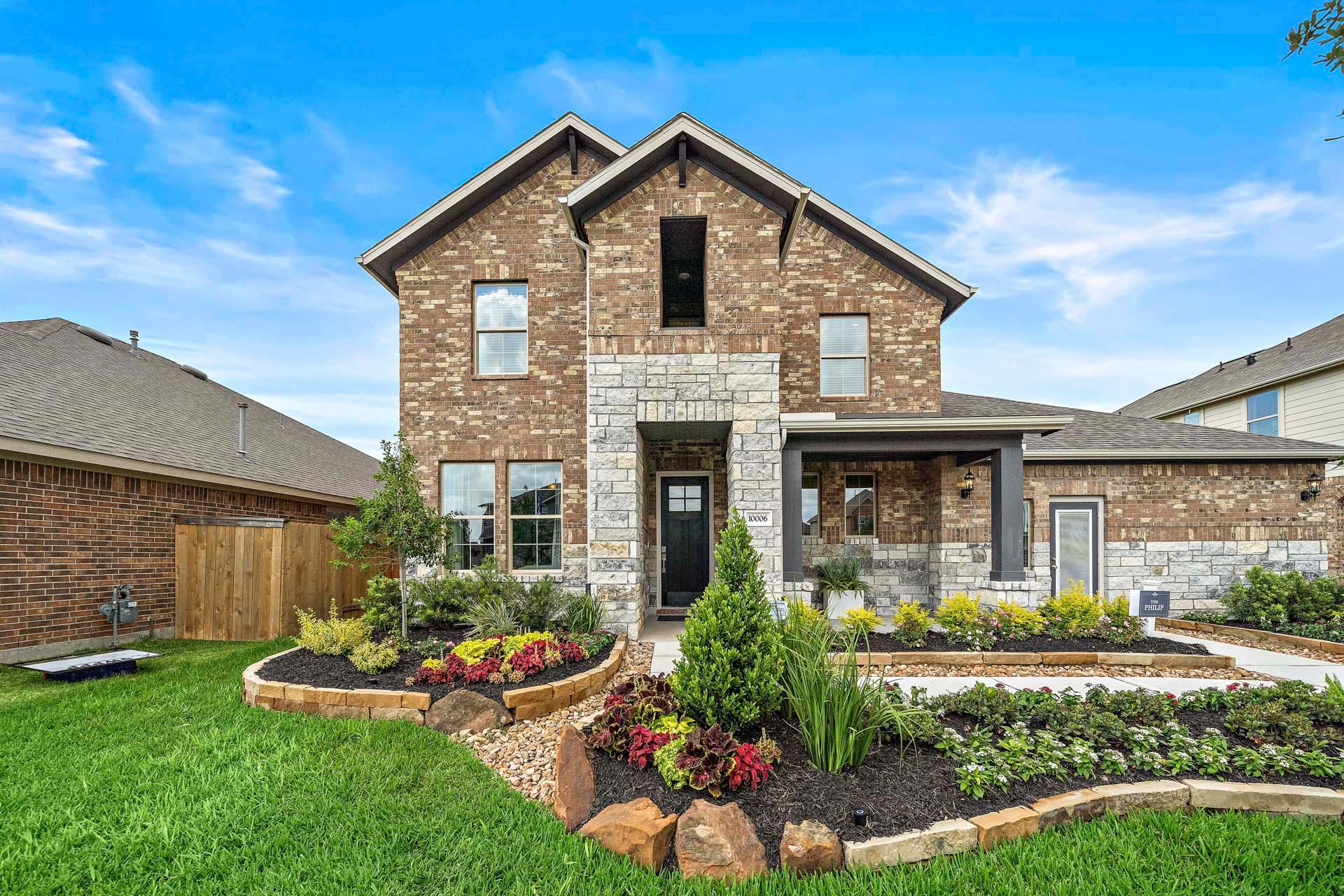 Two-story brick home exterior at Sierra Vista in Rosharon TX with stone accents, covered porch and vibrant landscaped yard