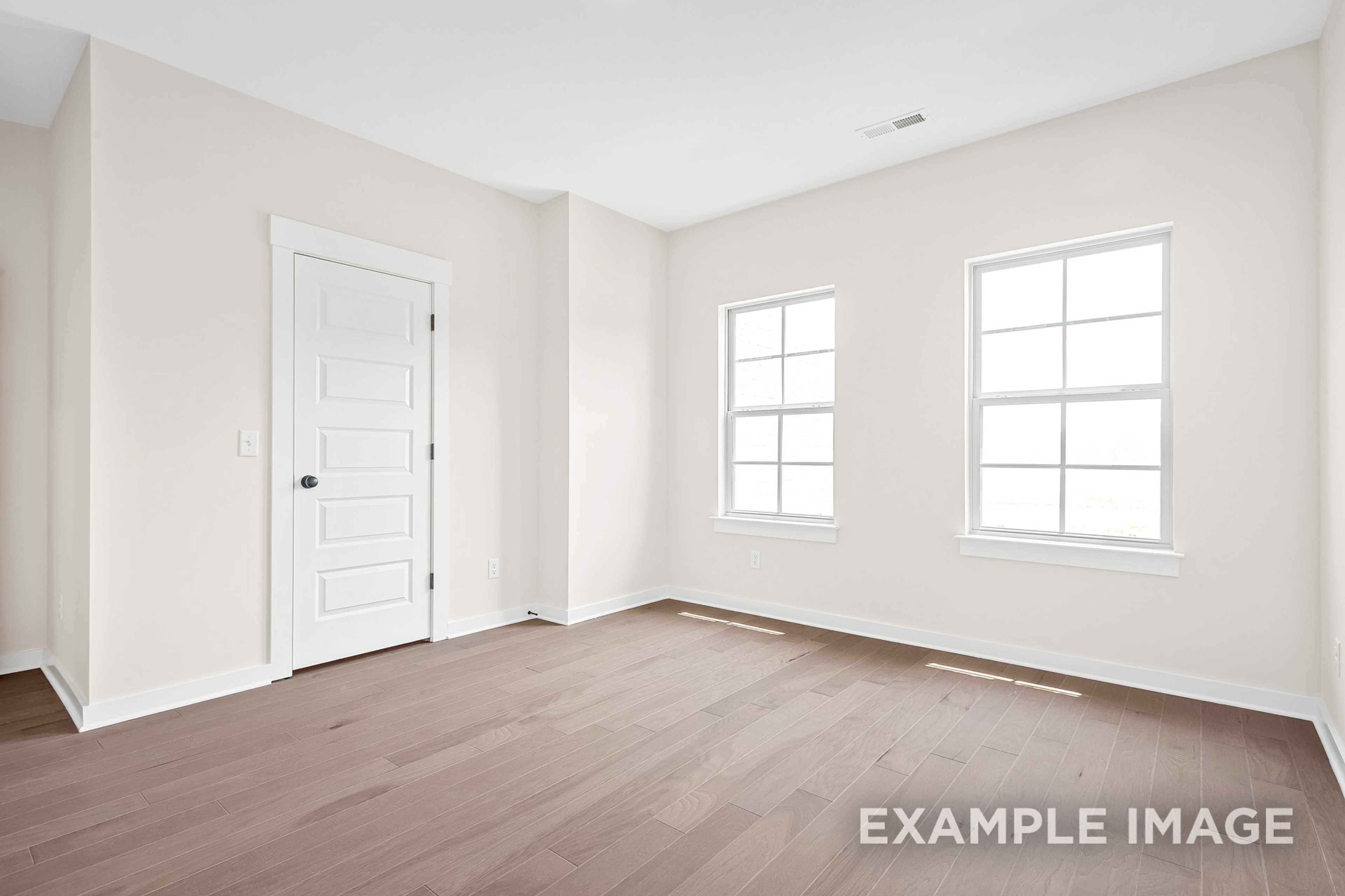 Spacious empty bedroom in The Hawkins with white walls, large windows, paneled door, and hardwood floors