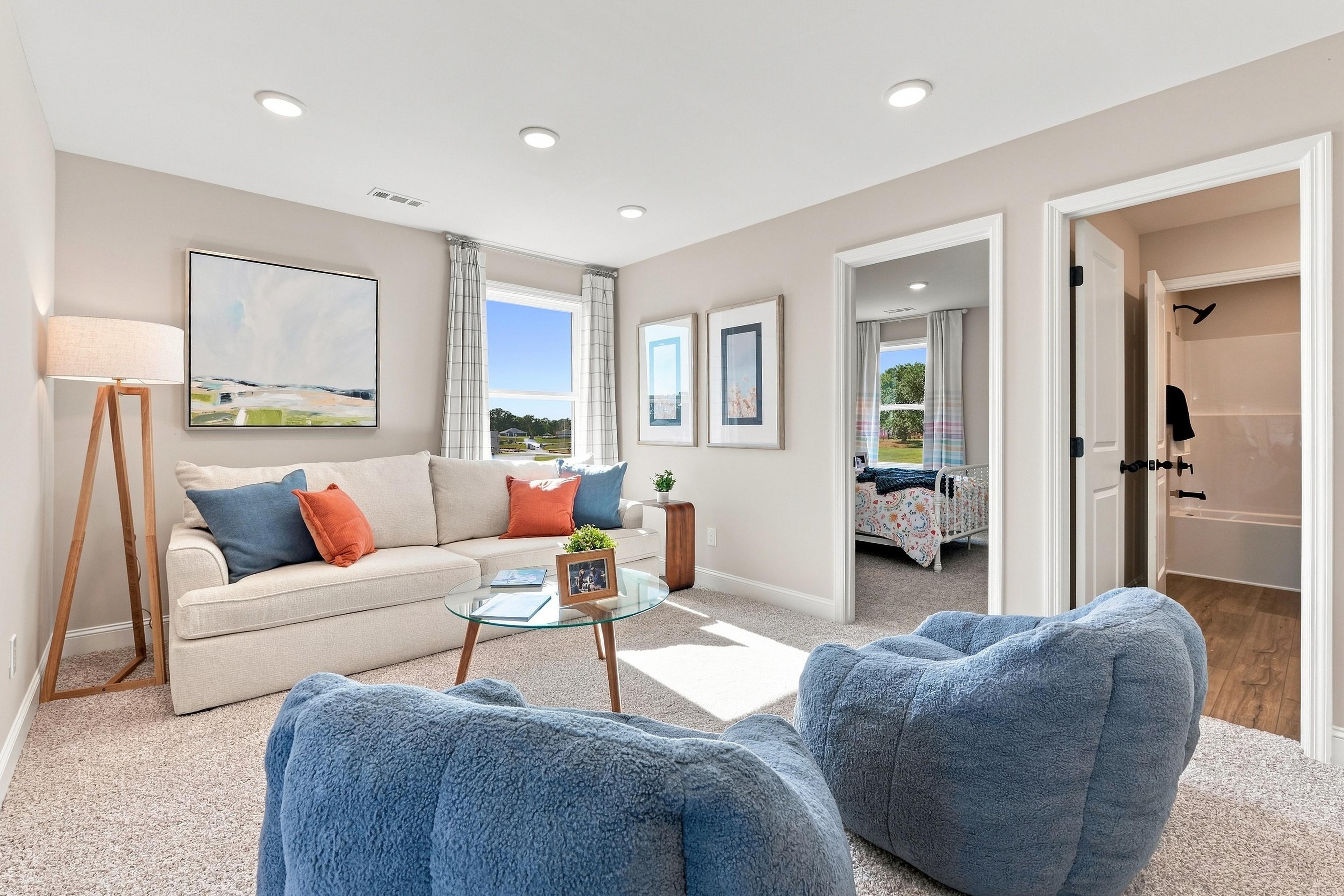 Bright bonus room with cream sofa and blue accent chairs at Bailey Park by Davidson Homes in Fayetteville, Tennessee