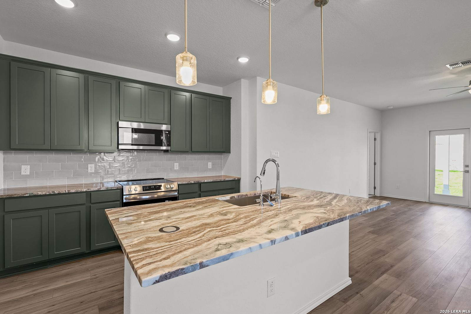 Modern kitchen with dark green cabinets, marble-style island, and pendant lighting in The Brazos B home in Agave, San Antonio.