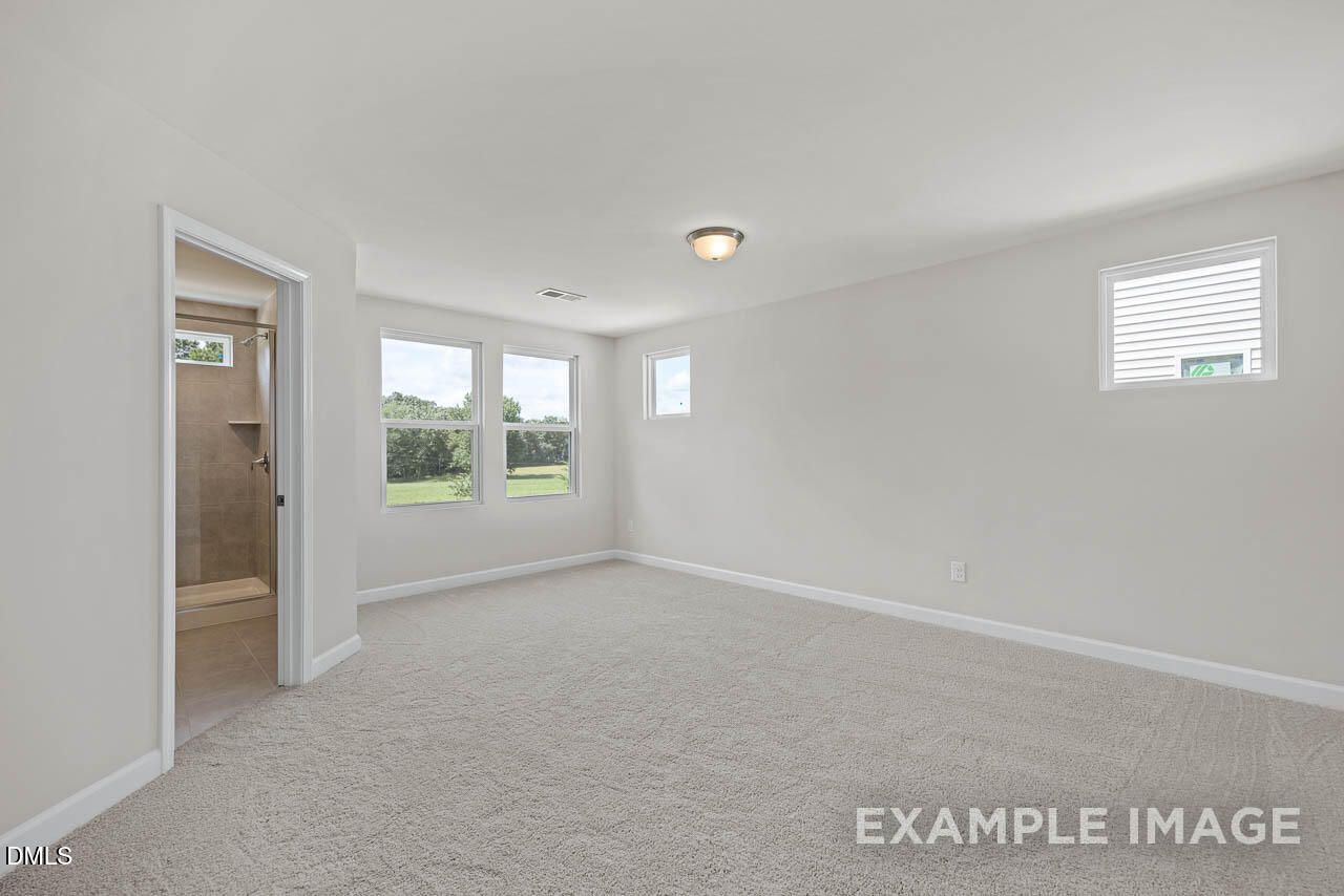 Bright primary bedroom with neutral carpet and en suite bathroom in The Graham floor plan at Springvale, Fuquay-Varina, NC.