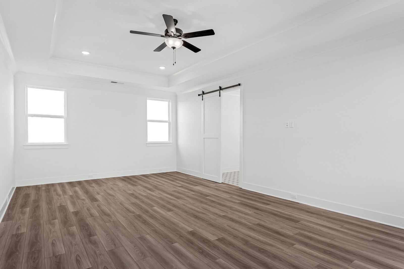 Bright bedroom with white walls, barn door, ceiling fan, and luxury vinyl plank flooring in The Alston A, Murfreesboro