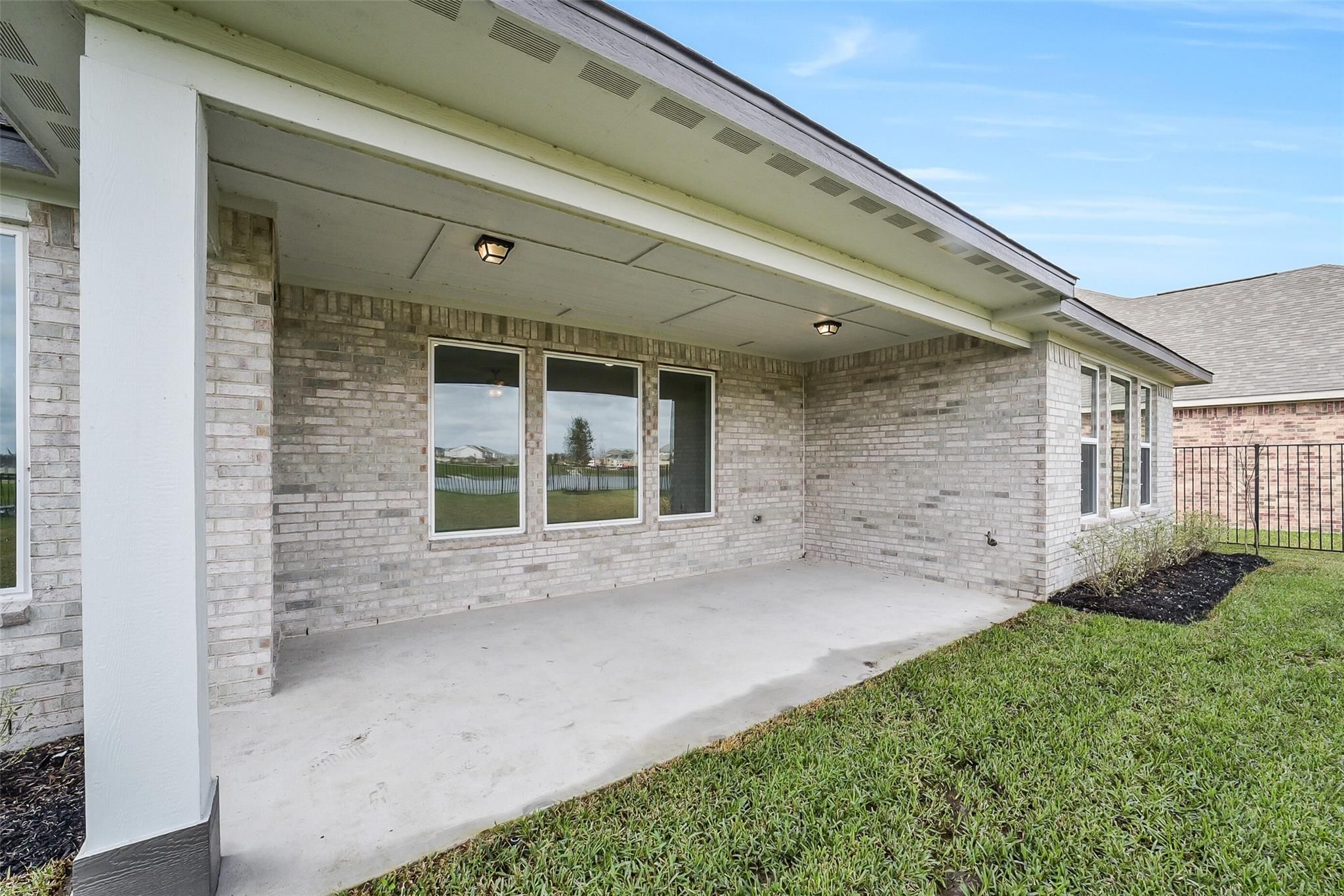 Covered patio with white brick exterior, large windows, and lush green yard in Davidson Homes The Philip B, Sierra Vista, Rosharon, Texas
