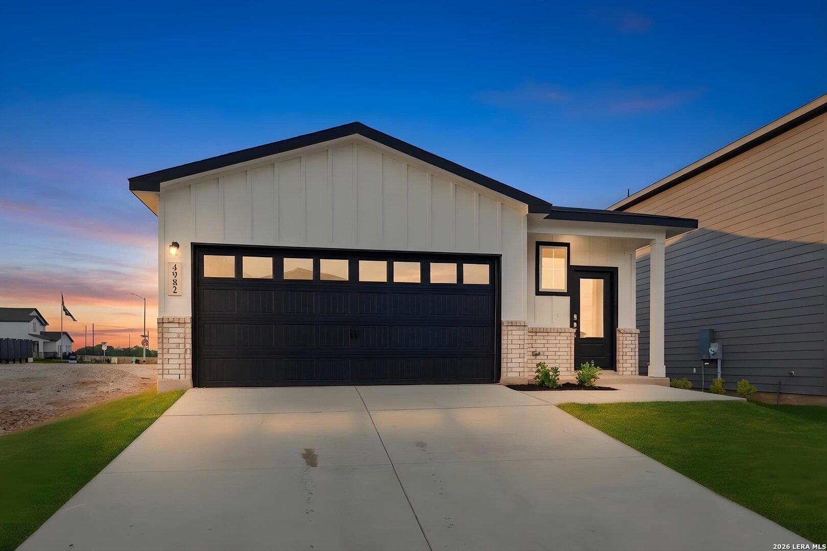 Modern white shiplap farmhouse with black 2-car garage and brick accents at dusk in Davidson Homes The Frio B, Agave, San Antonio